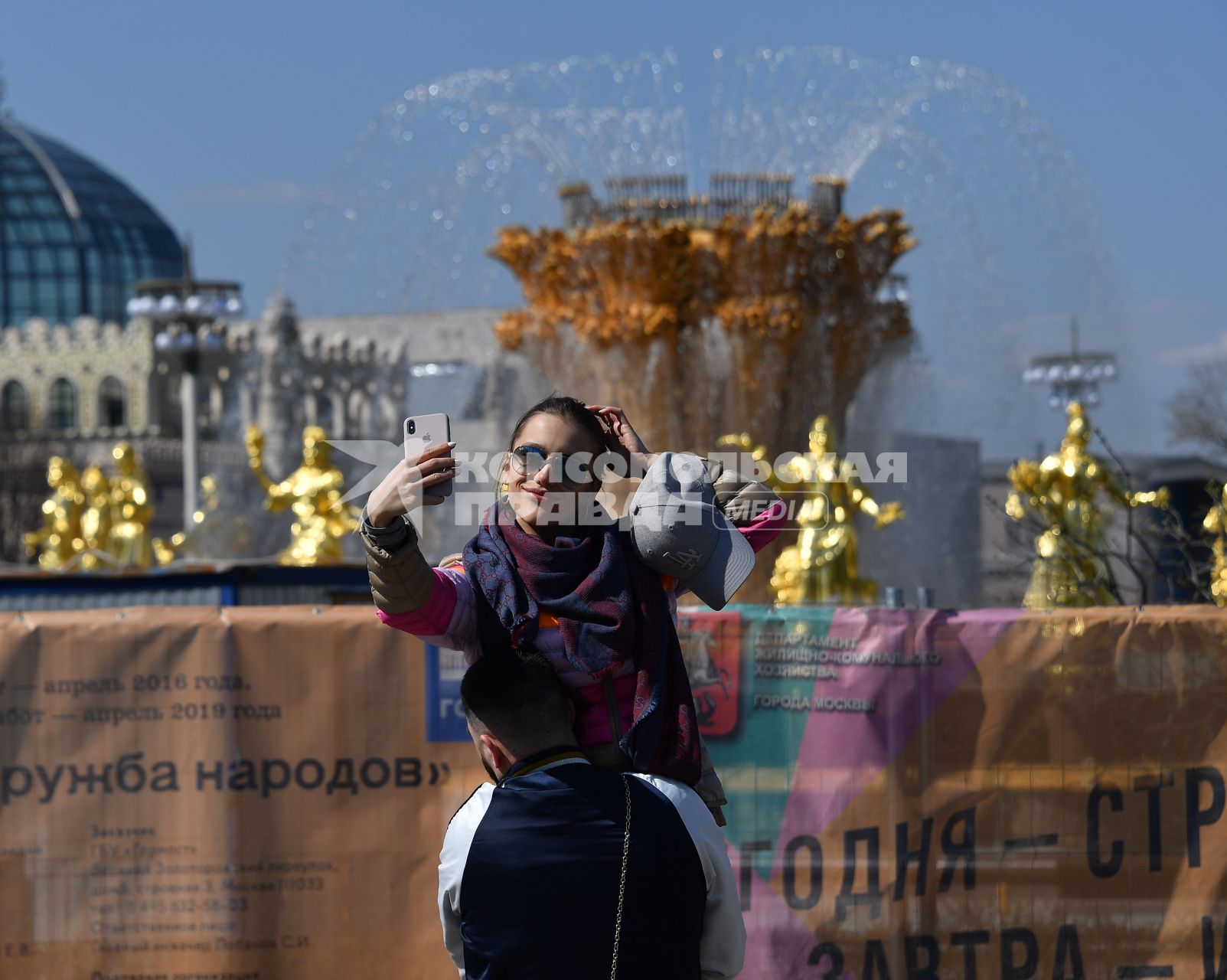 Москва. Девушка делает селфи на фоне фонтана `Дружба народов` на ВДНХ.
