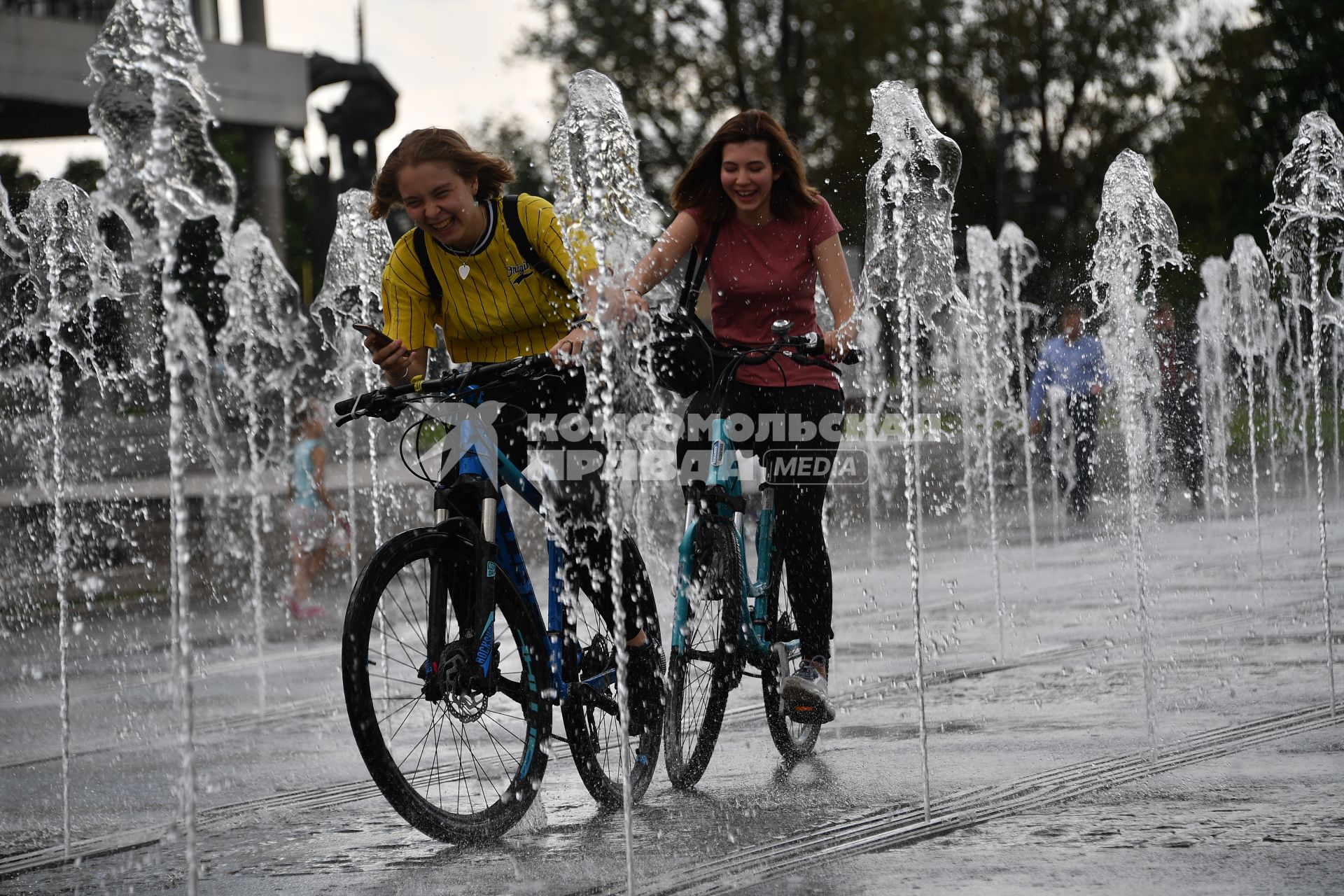 Москва.  Девушки катаются на велосипедах среди фонтанов  Крымской набережной.