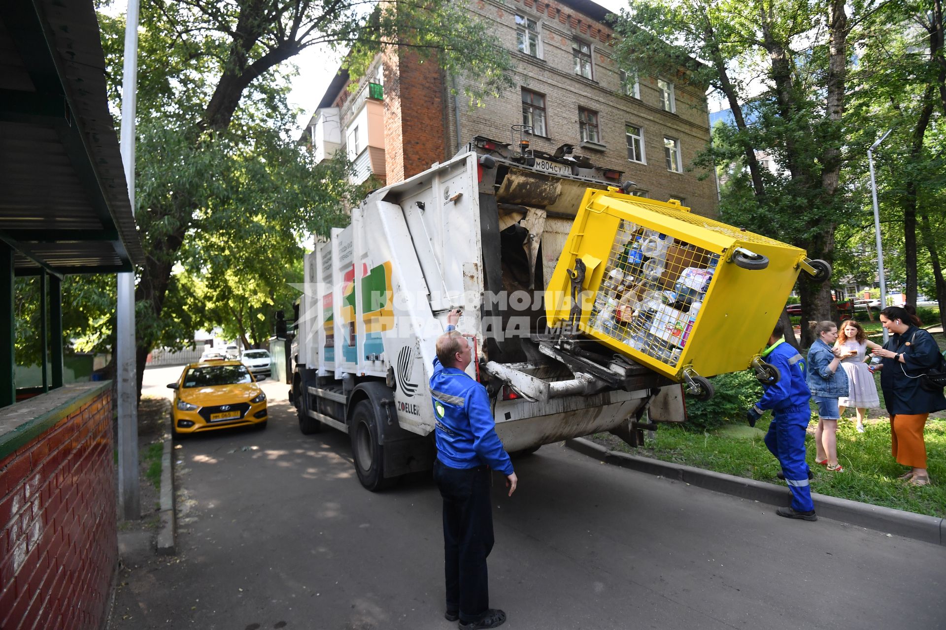 Москва.   Рабочие грузят мусорный контейнер.