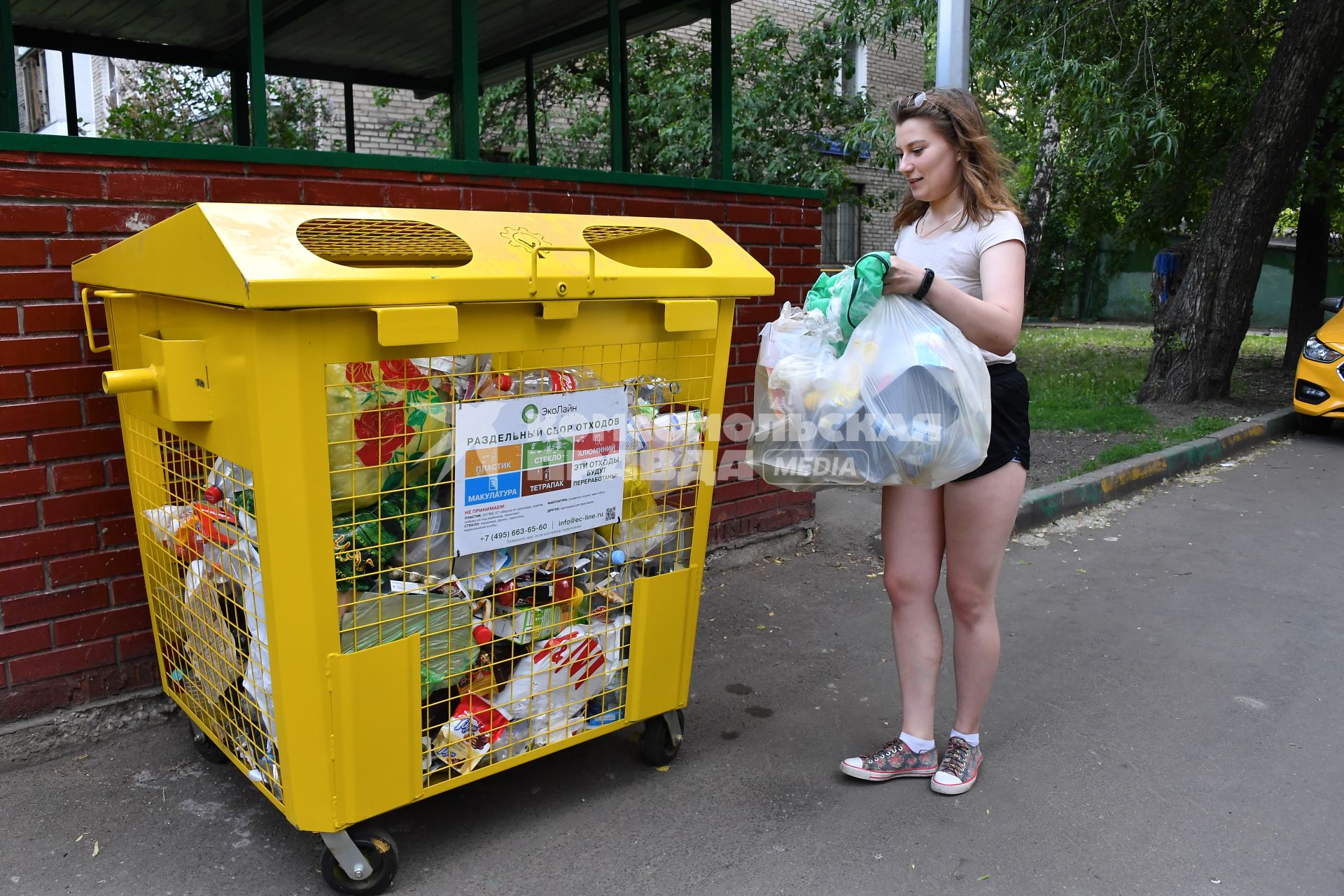 Москва.   Девушка выбрасывает мусор в мусорный контейнер.