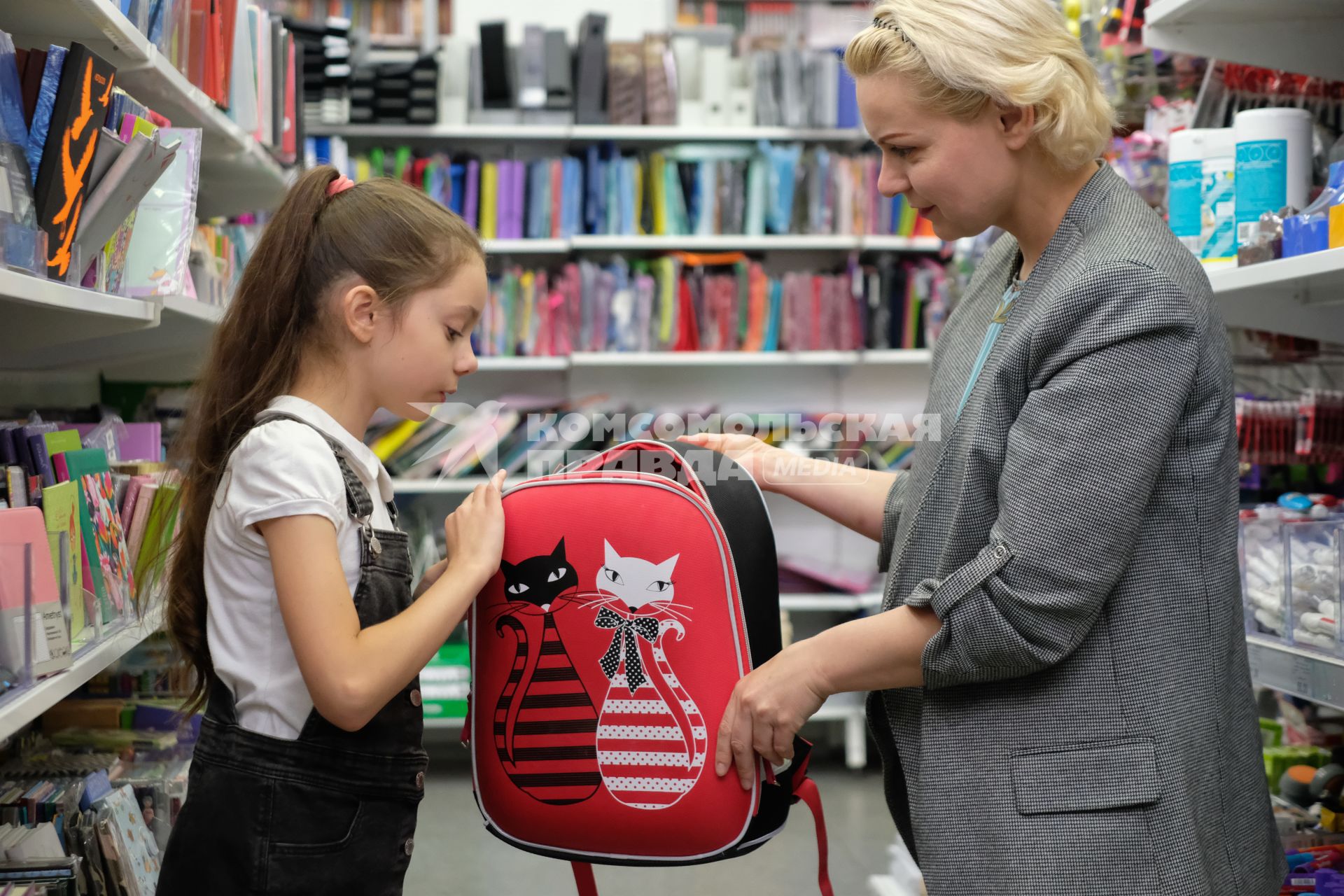 Санкт-Петербург.   Женщина с девочкой выбирают рюкзак в отделе школьных принадлежностей в магазине канцтоваров перед началом учебного года.