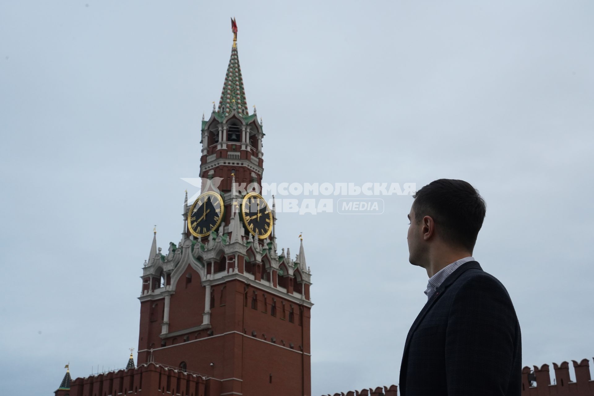 Москва.  Мужчина в костюме на Красной площади смотрит на Спасскую башню Кремля.