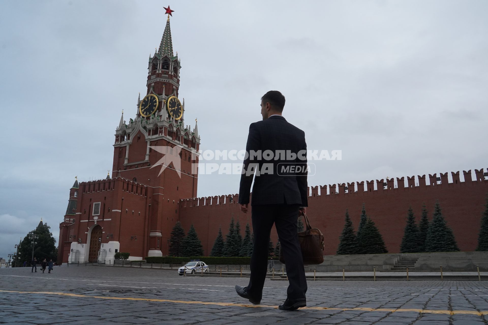 Москва.  Мужчина в костюме на Красной площади смотрит на Спасскую башню  Кремля.