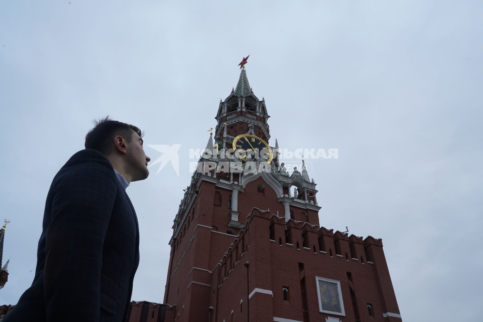 Москва.  Мужчина в костюме на Красной площади смотрит на Спасскую башню Кремля.