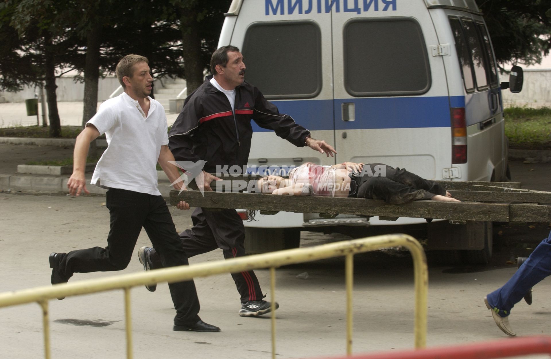 Захват заложников террористами в школе #1 города Беслан. Мужчины в гражданском несут на носилках освобожденную женщину-заложницу.