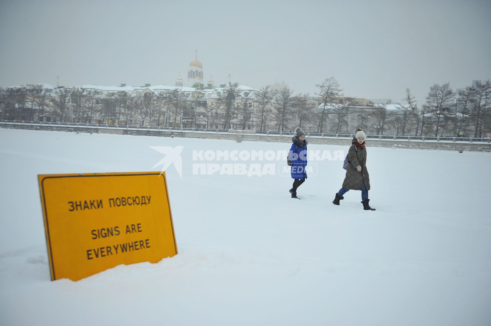 Екатеринбург. Дети идут по льду городского пруда мимо арт-объекта, дорожного знака с надписью \'Знаки повсюду\' во время снегопада