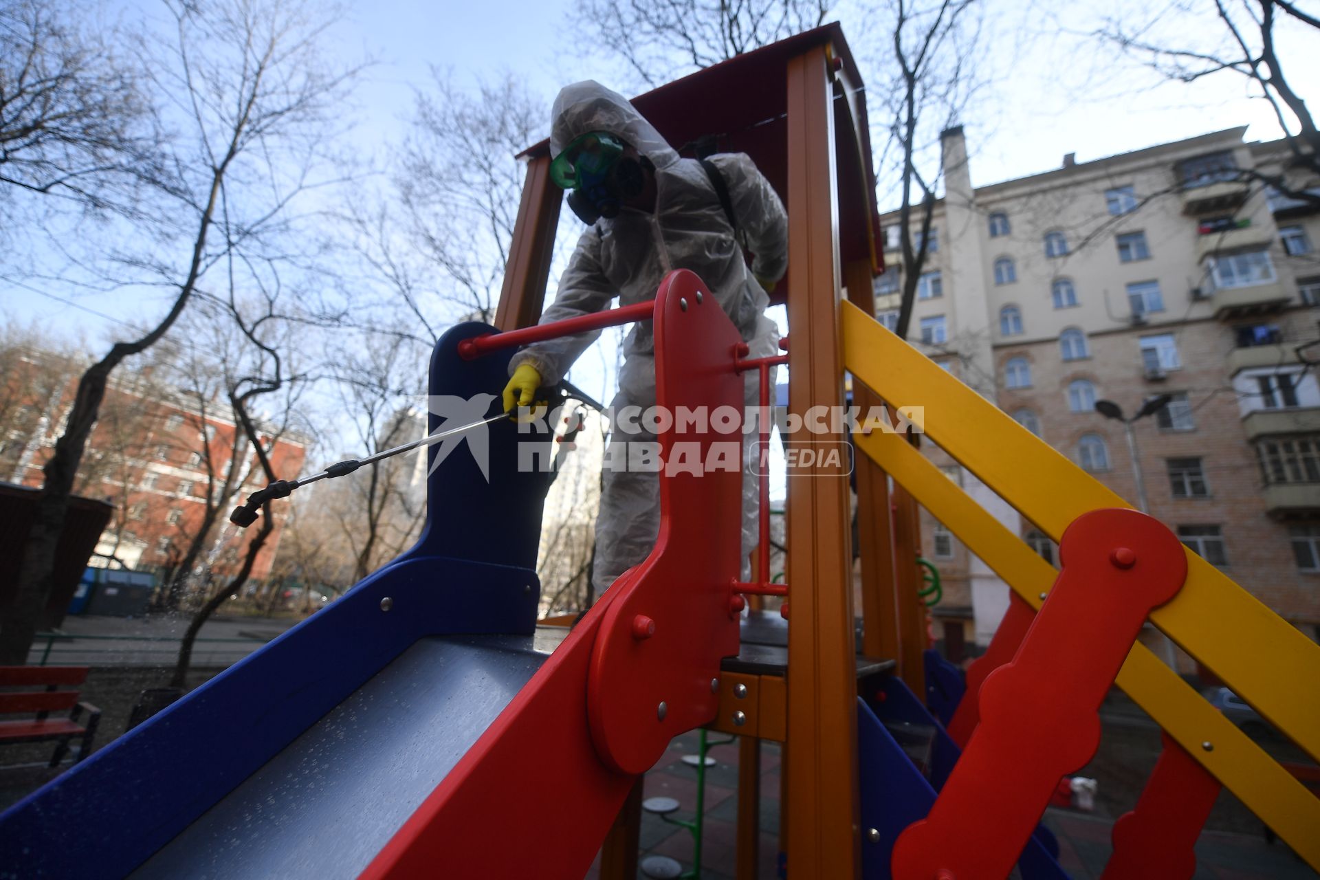 Москва. Сотрудник коммунальной службы в защитном костюме и респираторе во время дезинфекции детской площадки.