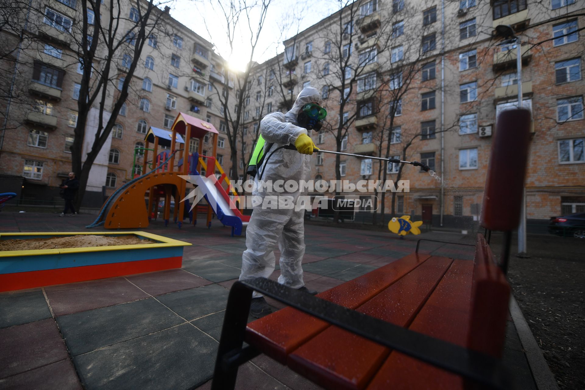 Москва. Сотрудник коммунальной службы в защитном костюме и респираторе во время дезинфекции детской площадки.