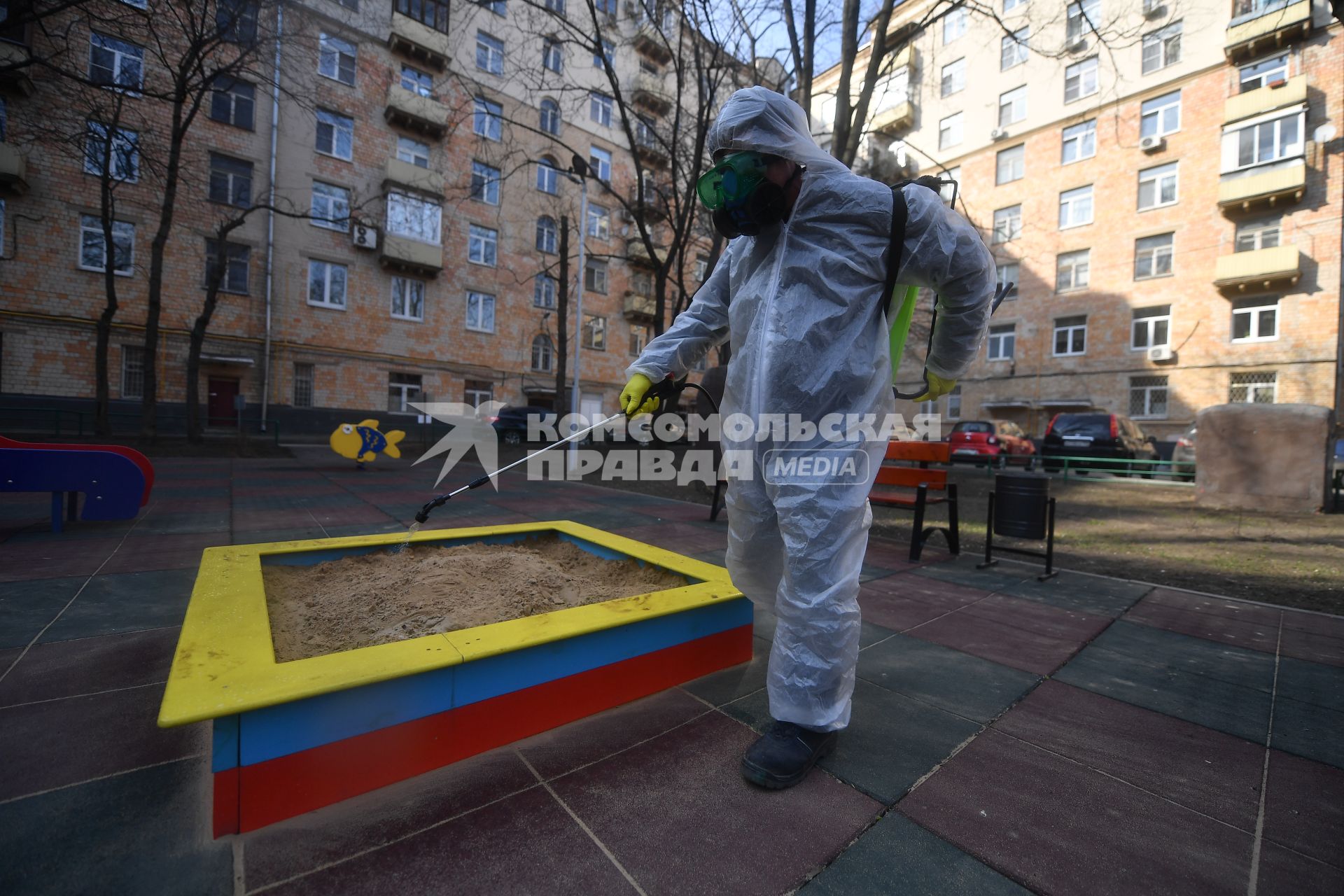 Москва. Сотрудник коммунальной службы в защитном костюме и респираторе во время дезинфекции детской площадки.