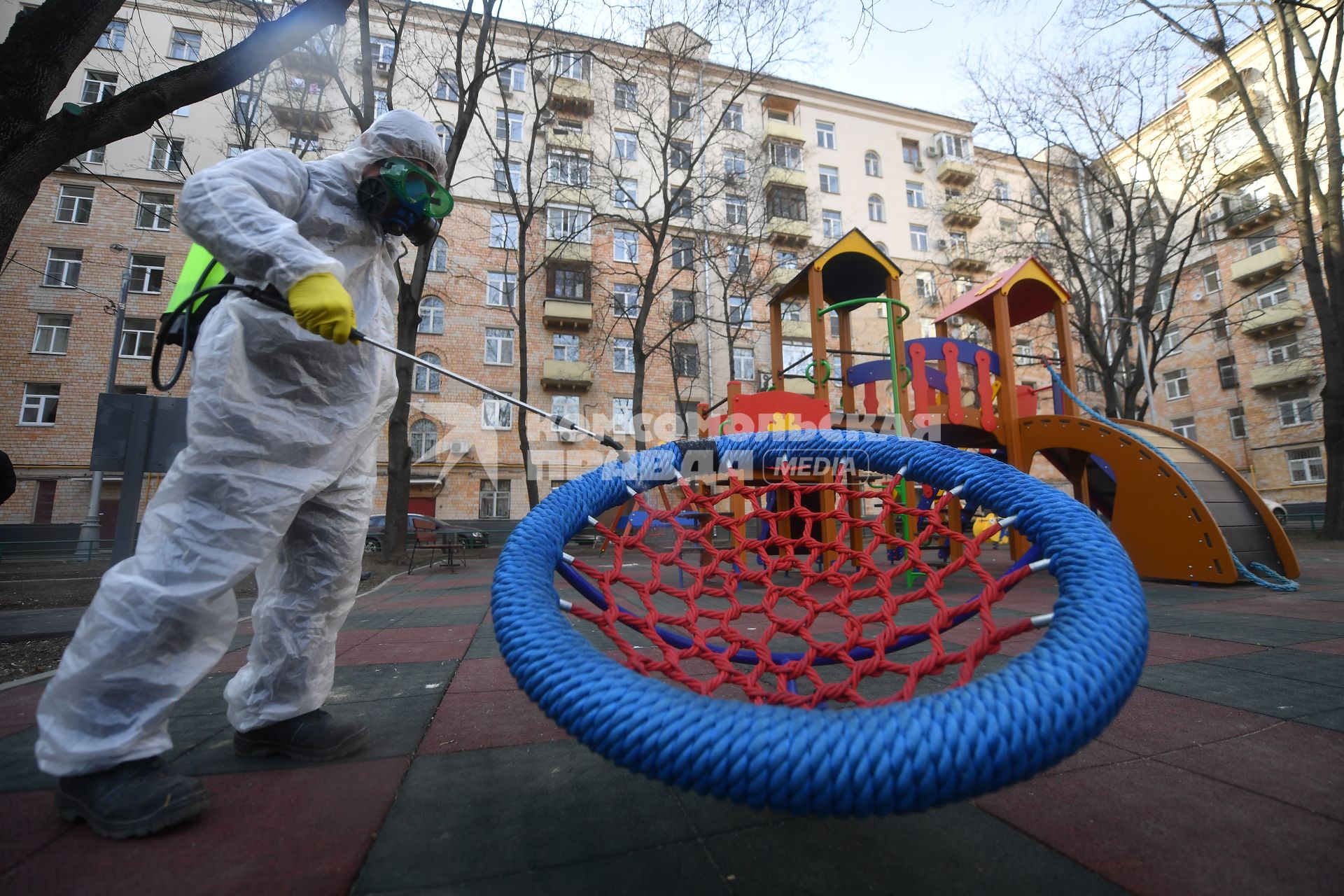 Москва. Сотрудник коммунальной службы в защитном костюме и респираторе во время дезинфекции детской площадки.