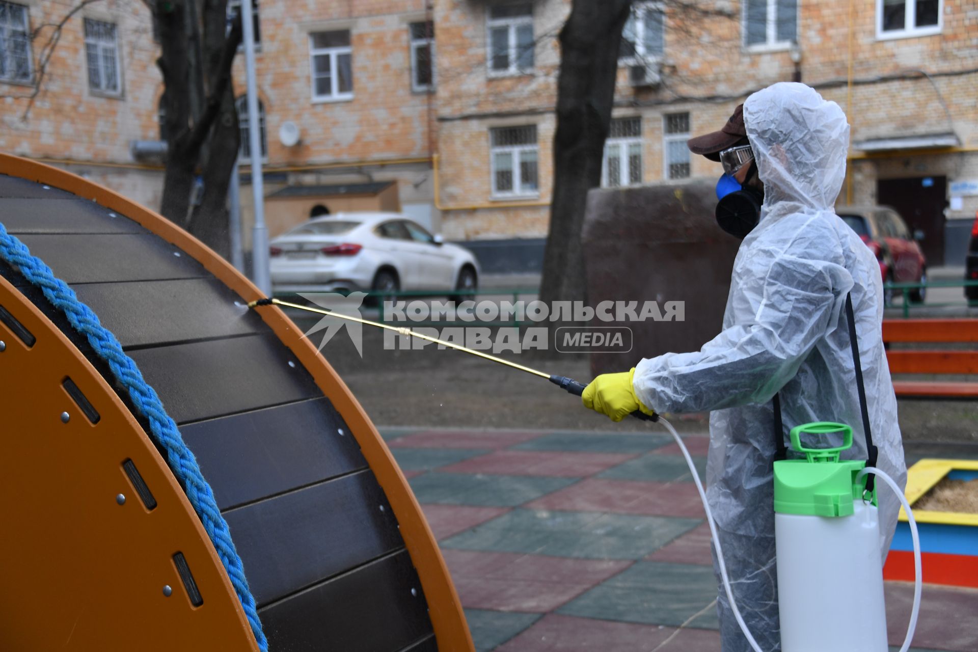 Москва. Сотрудник коммунальной службы в защитном костюме и респираторе во время дезинфекции детской площадки.