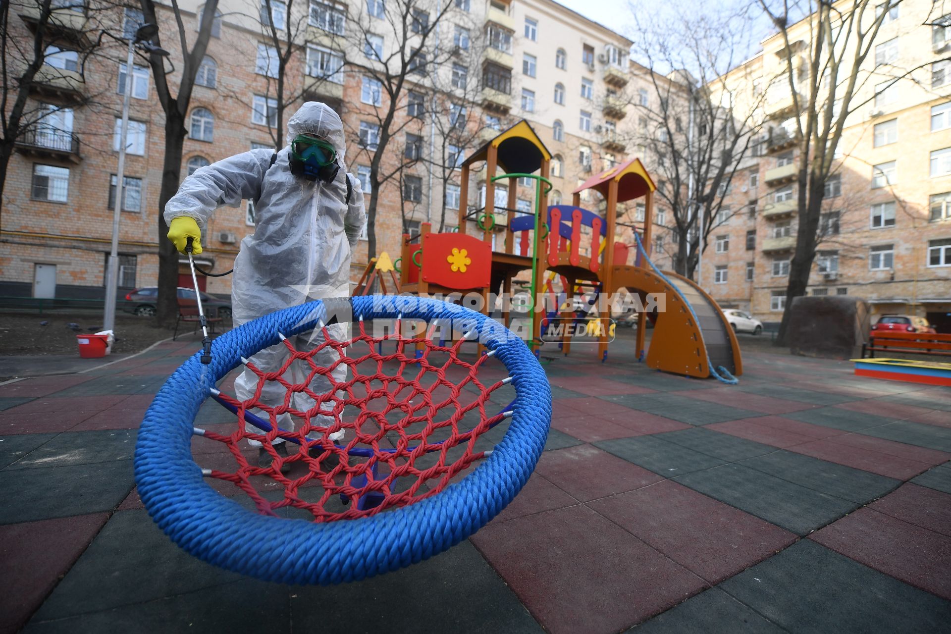 Москва. Сотрудник коммунальной службы в защитном костюме и респираторе во время дезинфекции детской площадки.