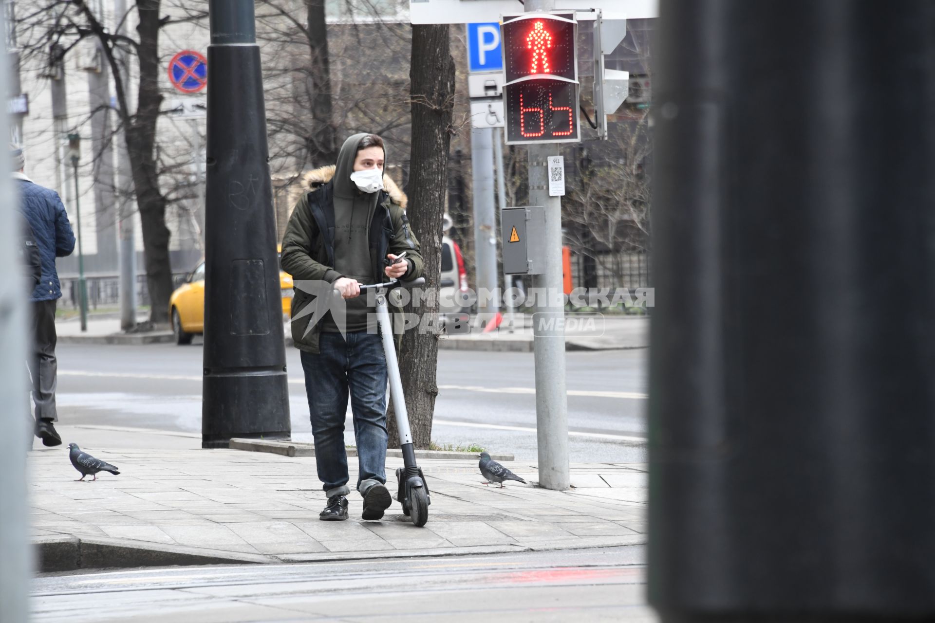 Москва. Мужчина на самокате в медицинской маске у пешеходного перехода.