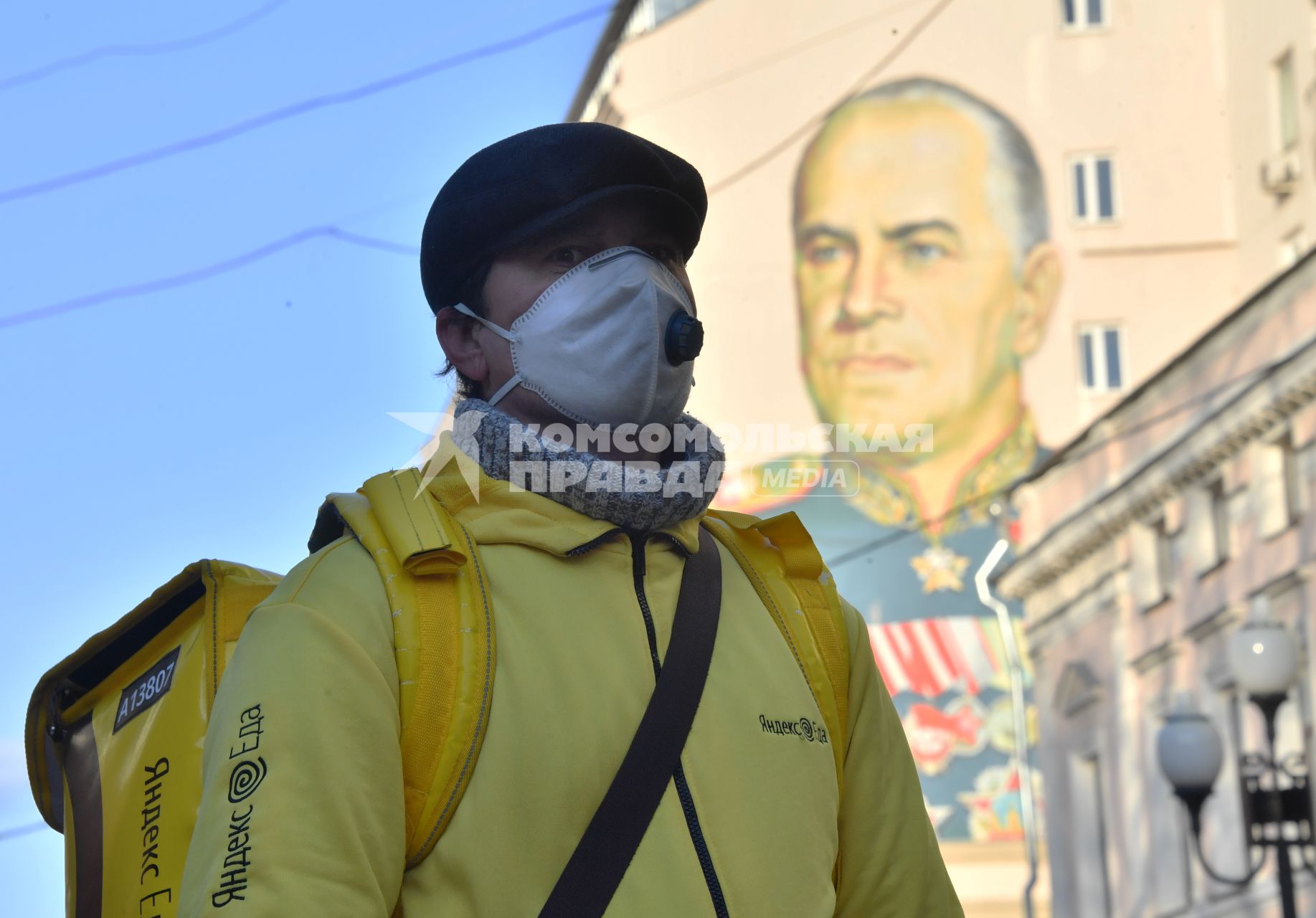 Москва. Сотрудник сервиса доставки еды  в медицинской маске у портрета  маршала Жукова.