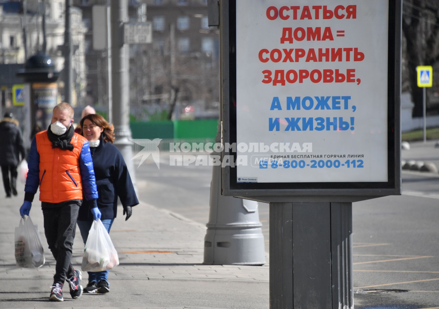 Москва. Прохожие на улице  на фоне плаката о самоизоляции.