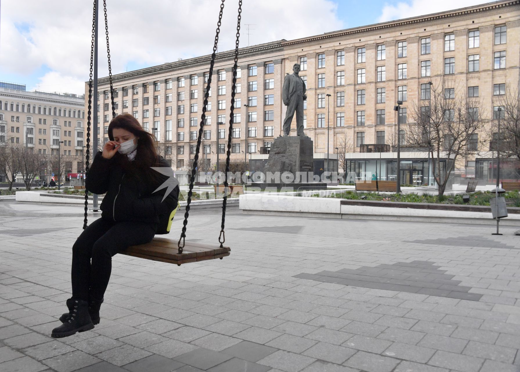 Москва. Девушка в медицинской маске сидит на качелях на Триумфальной площади у памятника Маяковскому.