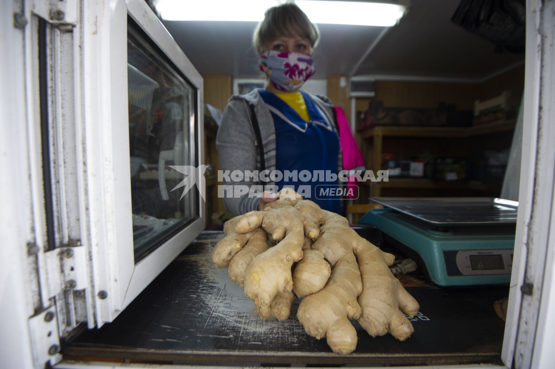 Екатеринбург. Продавщица в медицинской маске показывает корень имбиря во время эпидемии коронавирусной инфекции COVID-19