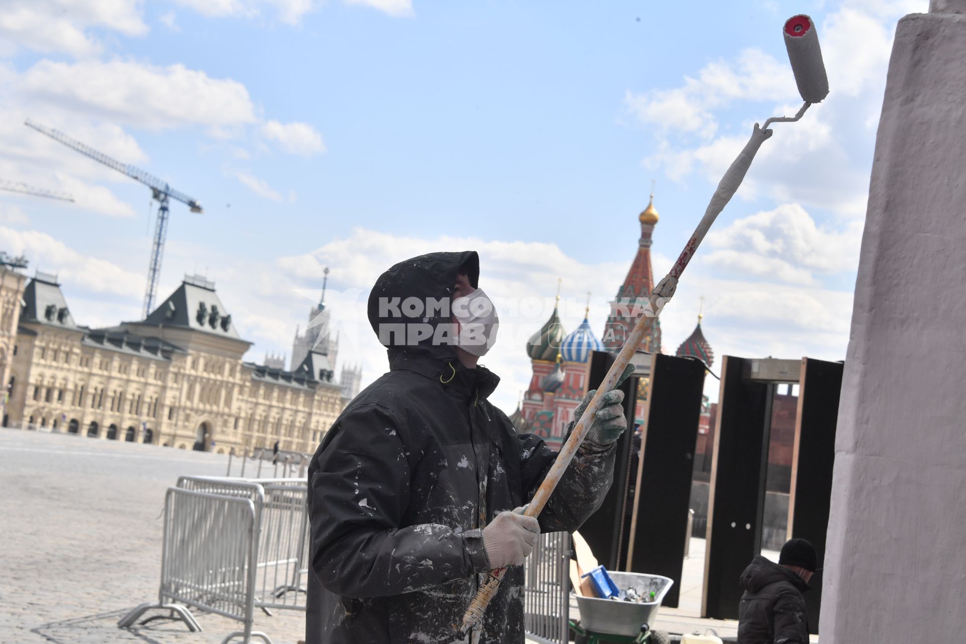 Москва. Рабочий в медицинской маске красит стену дома.