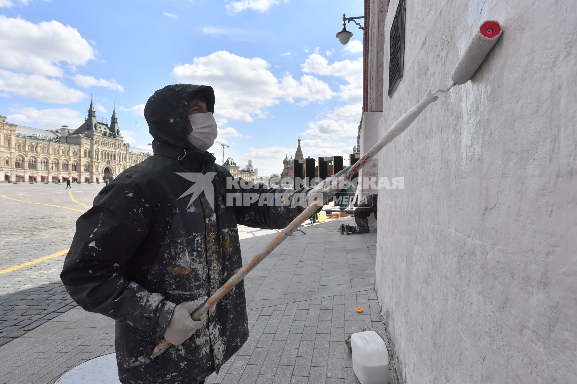 Москва. Рабочий в медицинской маске красит стену дома.