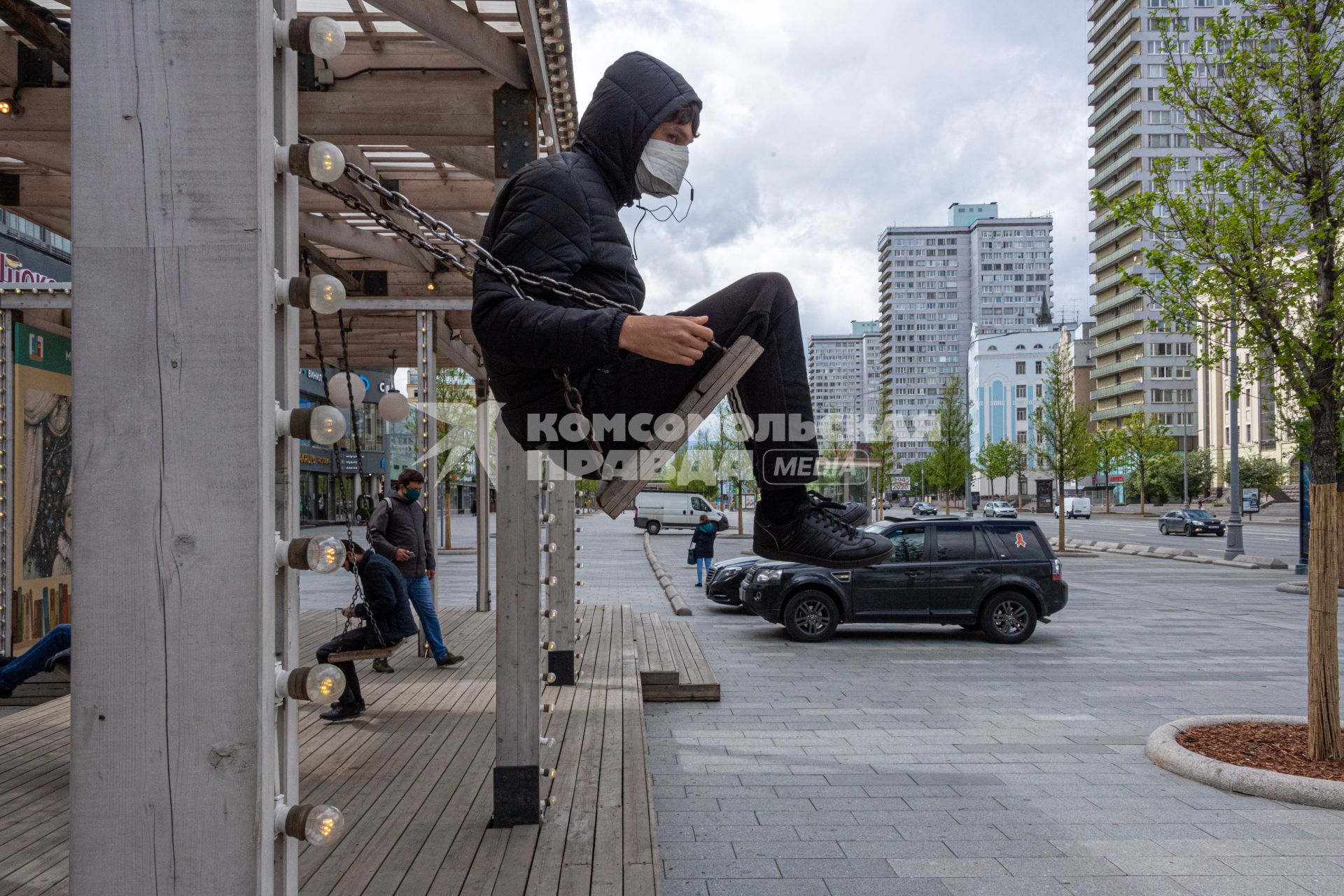 Москва. Молодой человек в медицинской маске на качелях на Новом Арбате.