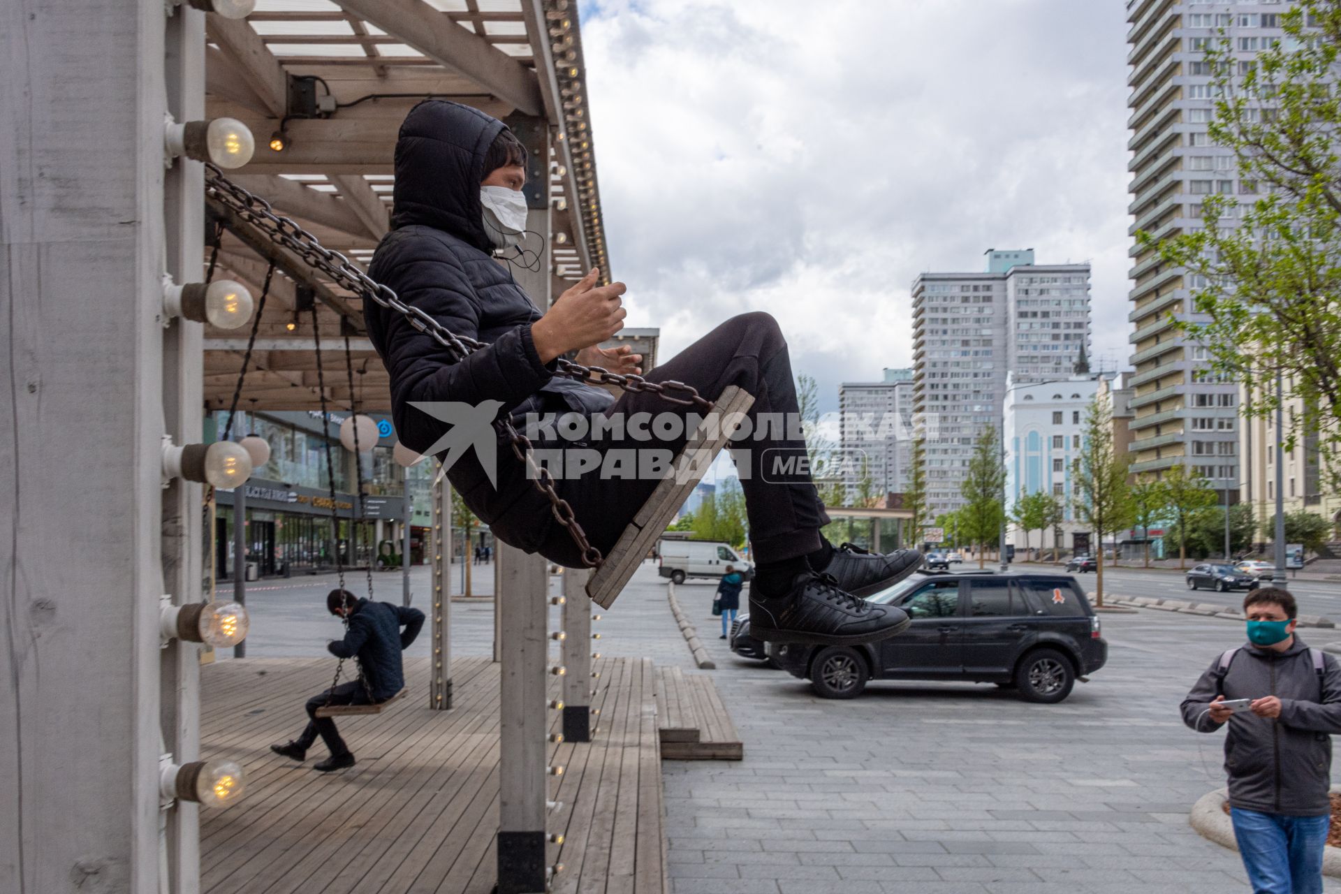 Москва. Молодой человек в медицинской маске на качелях на Новом Арбате.