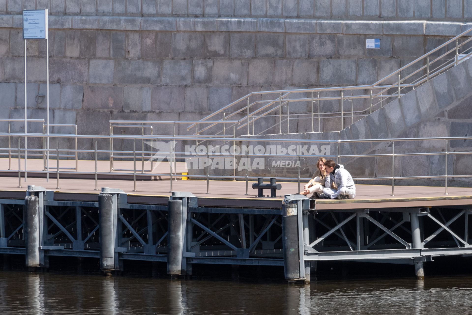 Москва. Молодые люди сидят на пристани Большого Каменного моста на Берсеневской набережной.