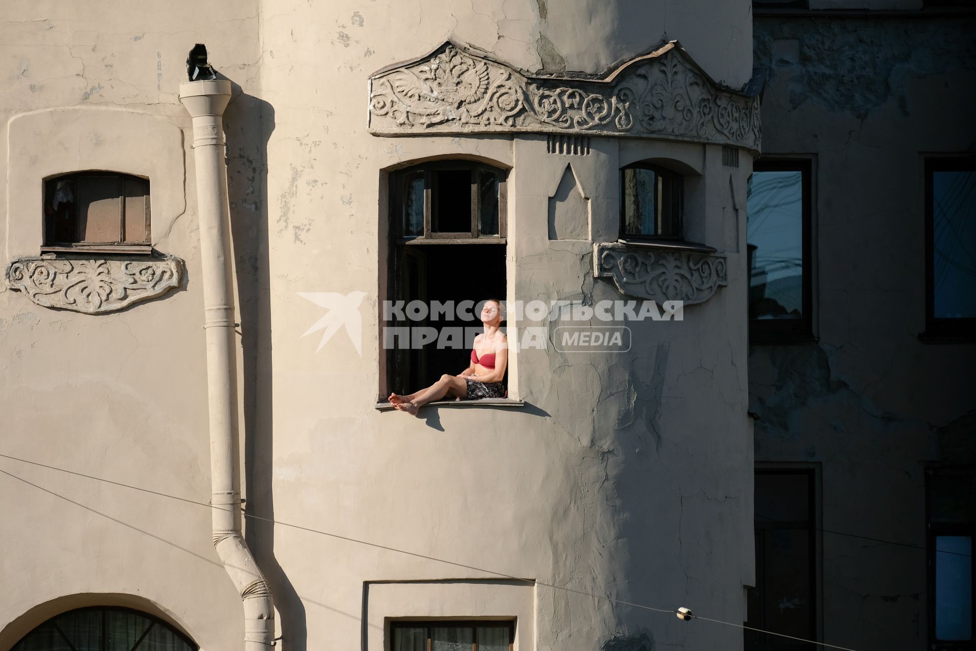 Санкт-Петербург.  Девушка загорает в окне.