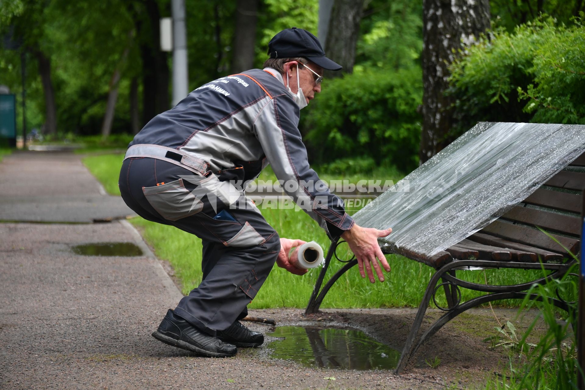 Москва.  Сотрудник парка обматывает скамейки пленкой.