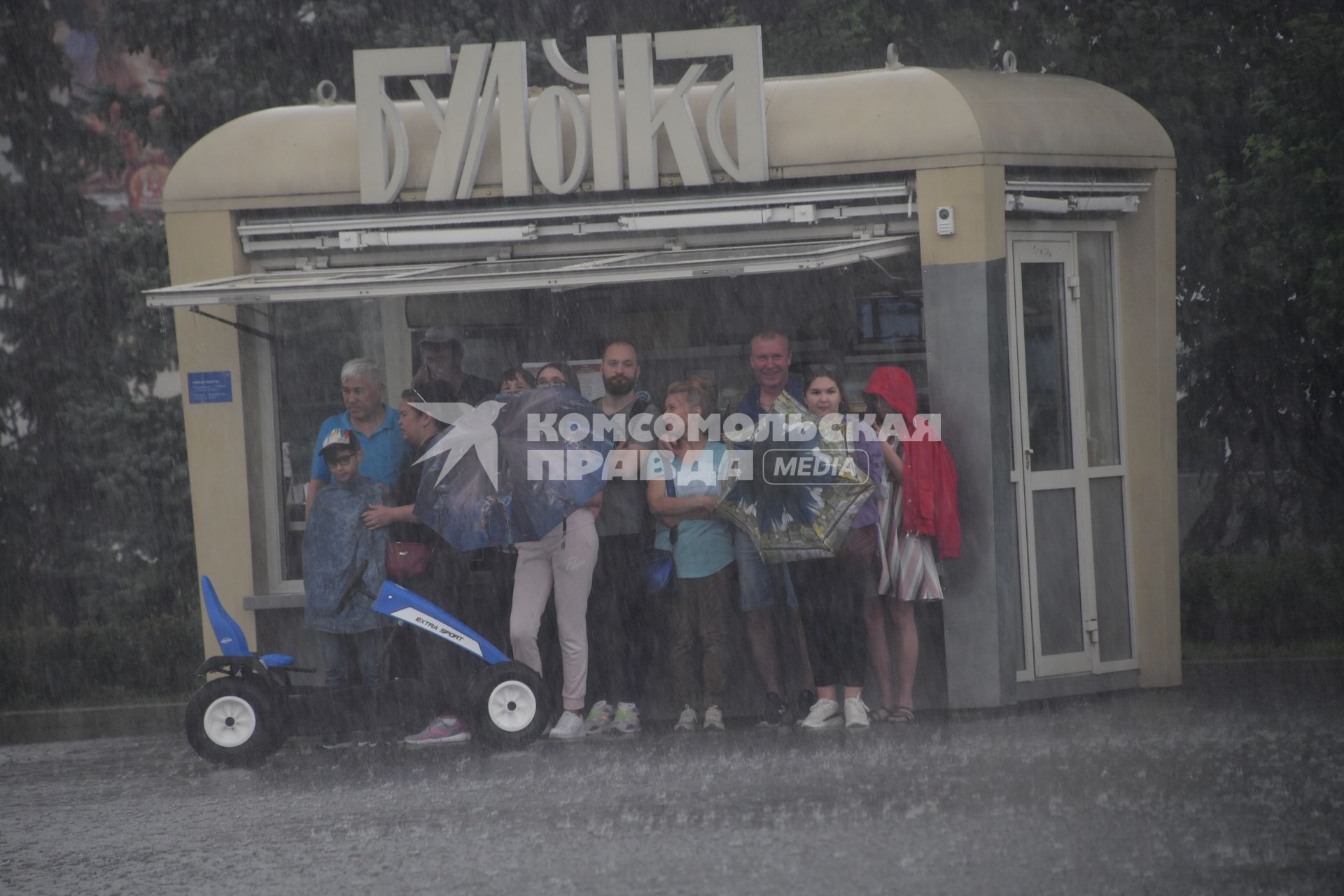 Москва.   Прохожие прячутся от дождя под козырьком павильона.