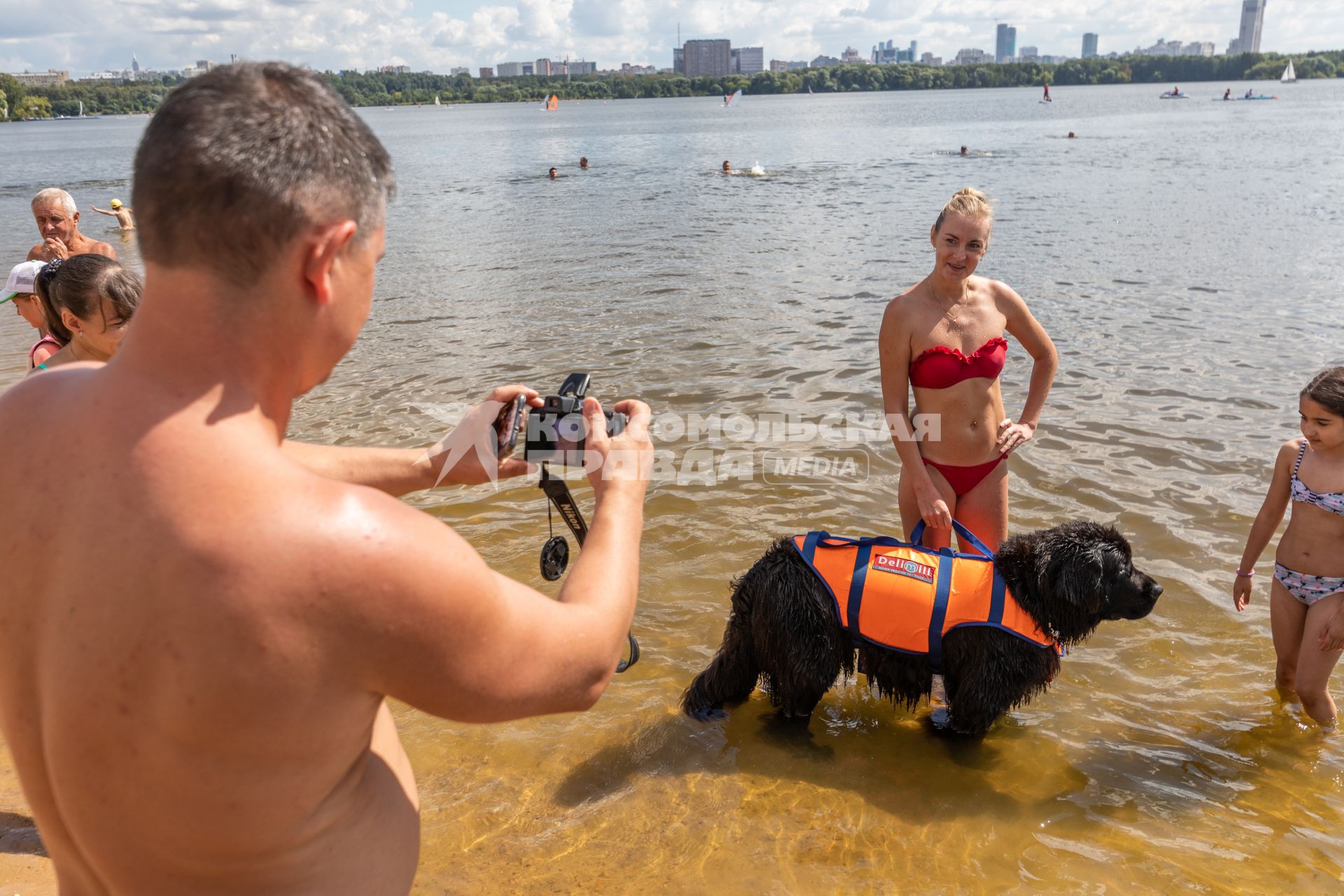 Москва. Мужчина фотографирует собаку породы ньюфаундленд на пляже.