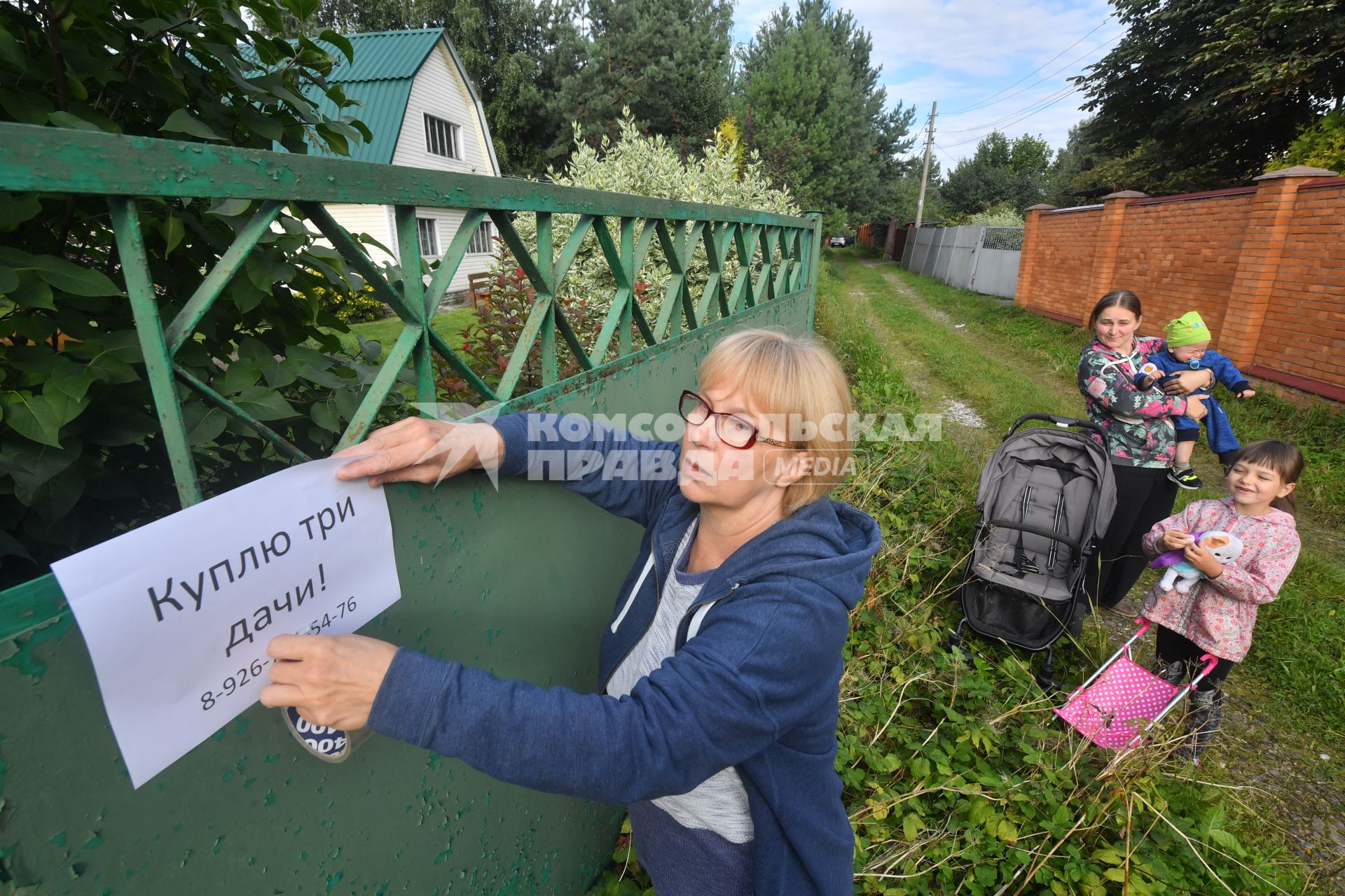 Московская область. Женщина вешает объявление о покупке дачи.