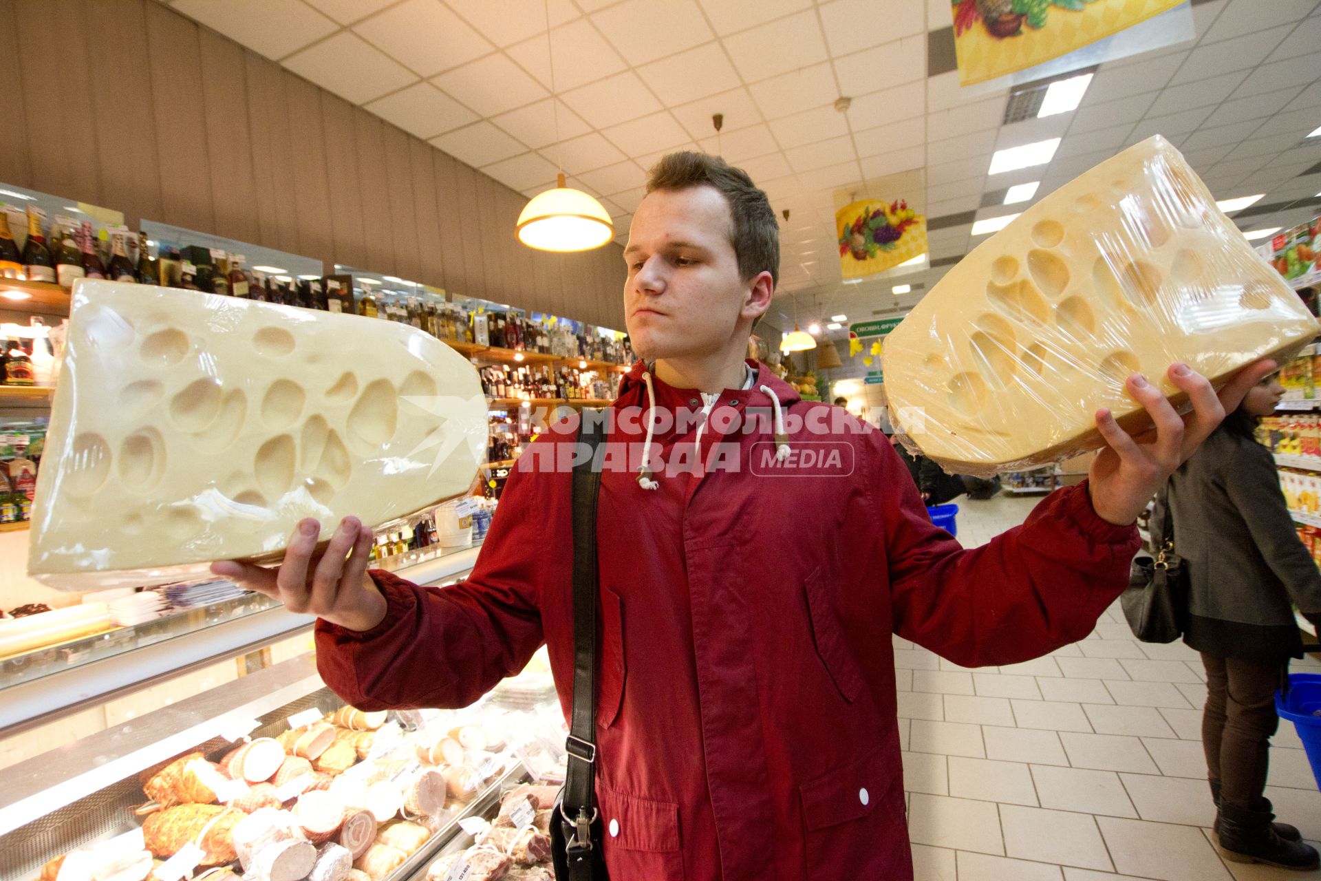 Белоруссия. Минск. Молодой человек держит в руках сыр в магазине.