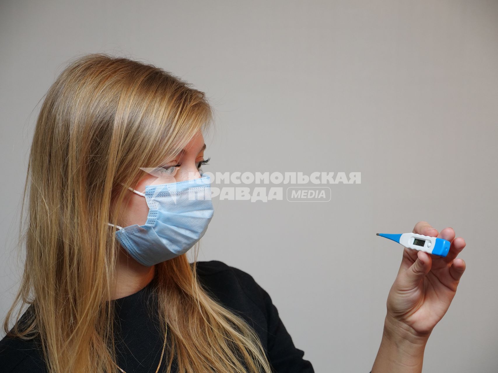 Самара.   Девушка в медицинской маске держит в руке электронный градусник.