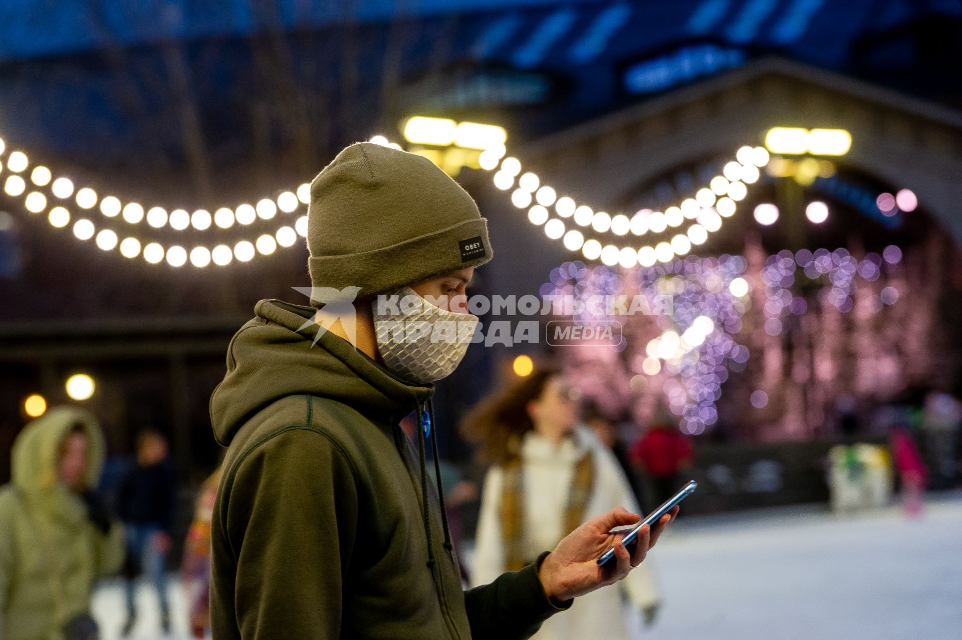 Санкт-Петербург.  Молодой человек в защитной маске с мобильным телефоном руке.