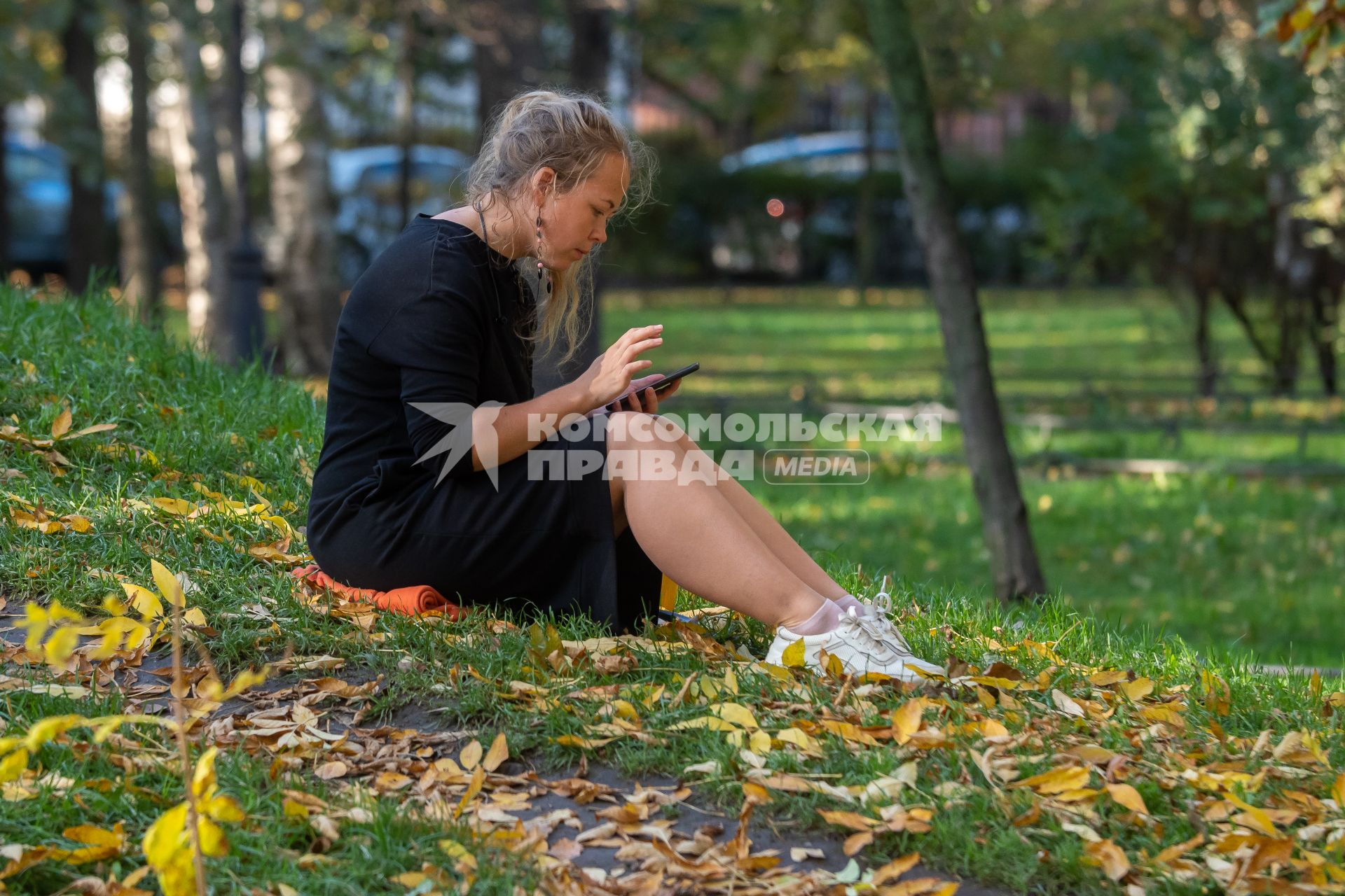 Санкт-Петербург. Девушка с мобильным телефоном сидит на земле в Михайловском саду.