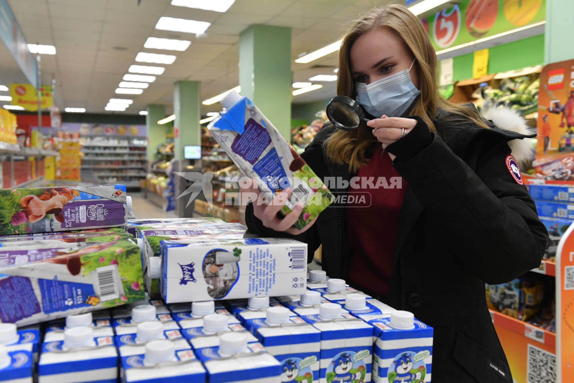 Москва.  Девушка в медицинской маске в магазине изучает пакет молока.