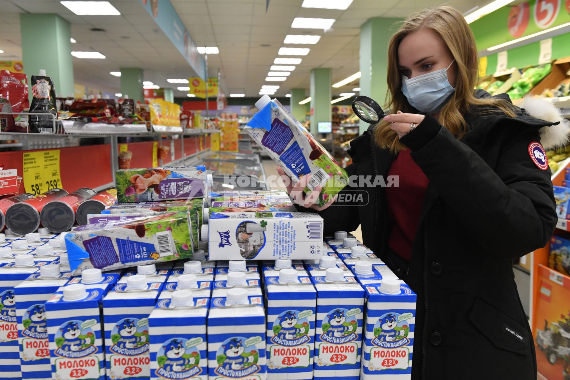 Москва.  Девушка в медицинской маске в магазине изучает пакет молока.