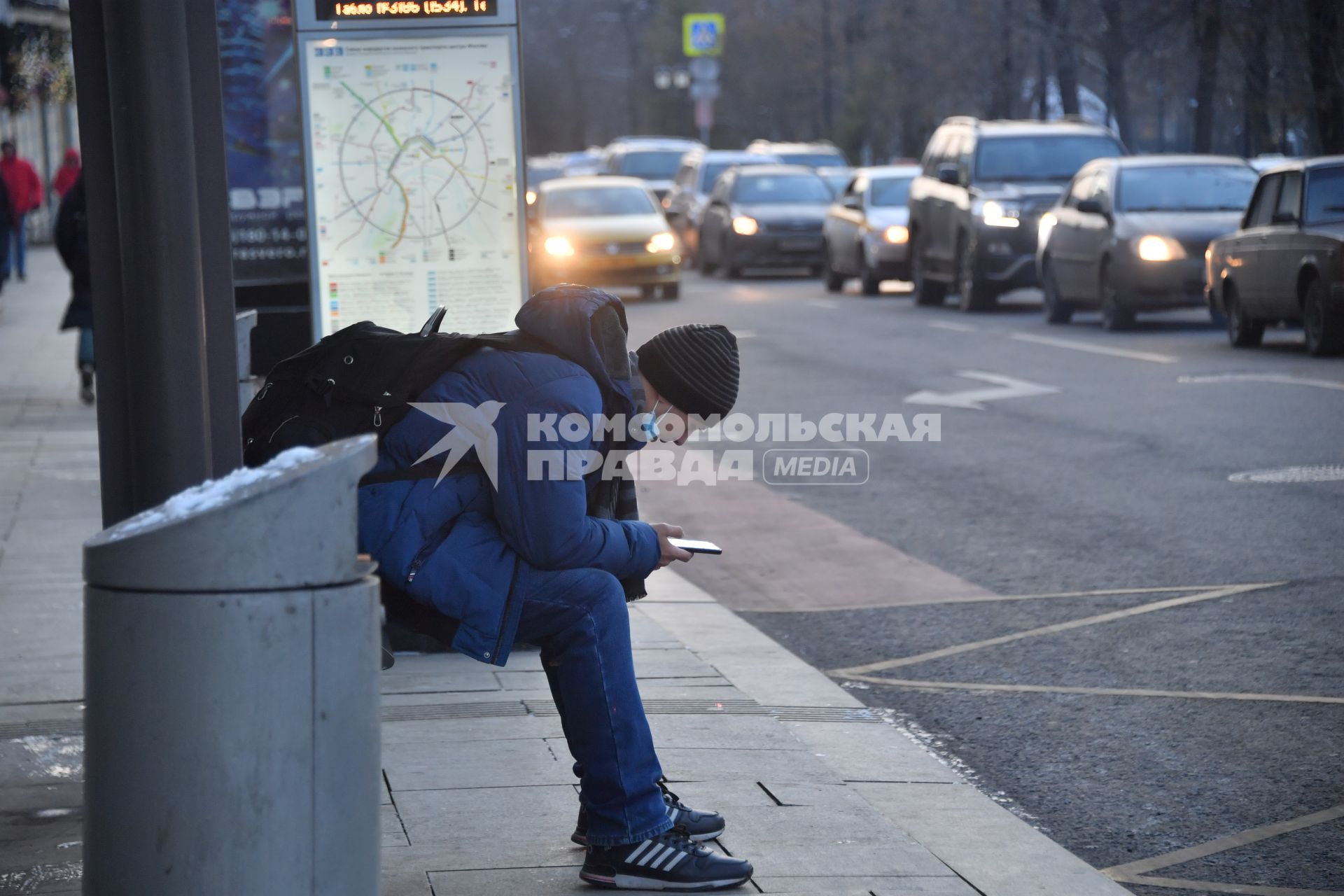 Москва.   Молодой человек с мобильным телефоном на остановке общественного транспорта.