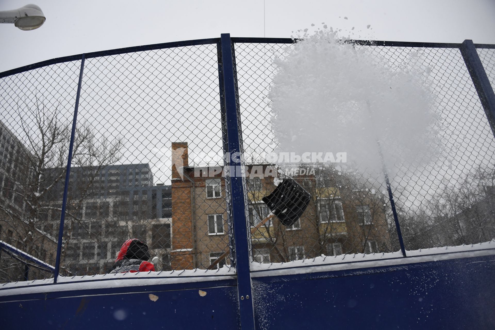 Москва.  Дворник чистит снег на хоккейной коробке.