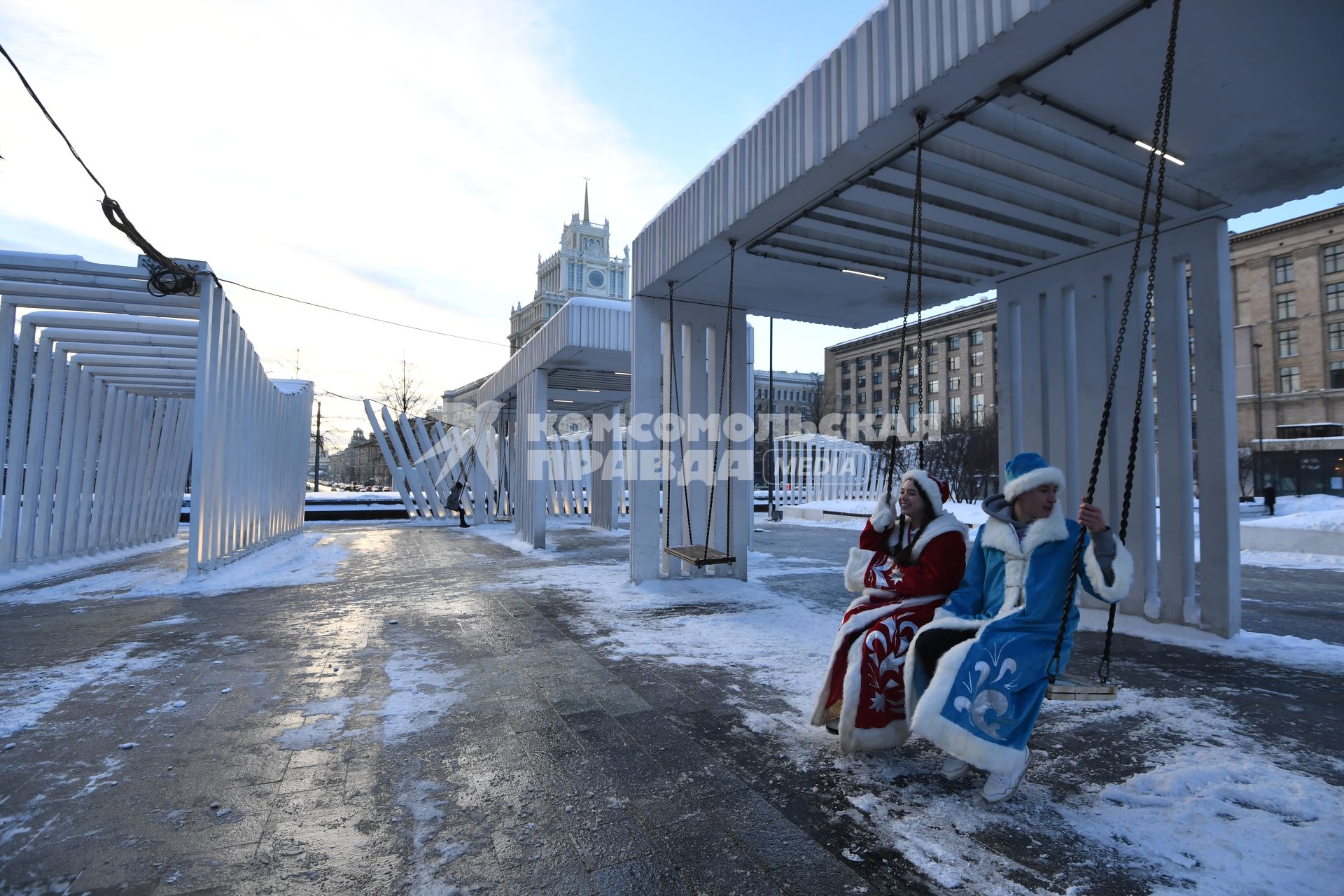 Москва.   Мужчина и женщина в костюмах деда Мороза и Снегурочки на качелях на Триумфальной площади.