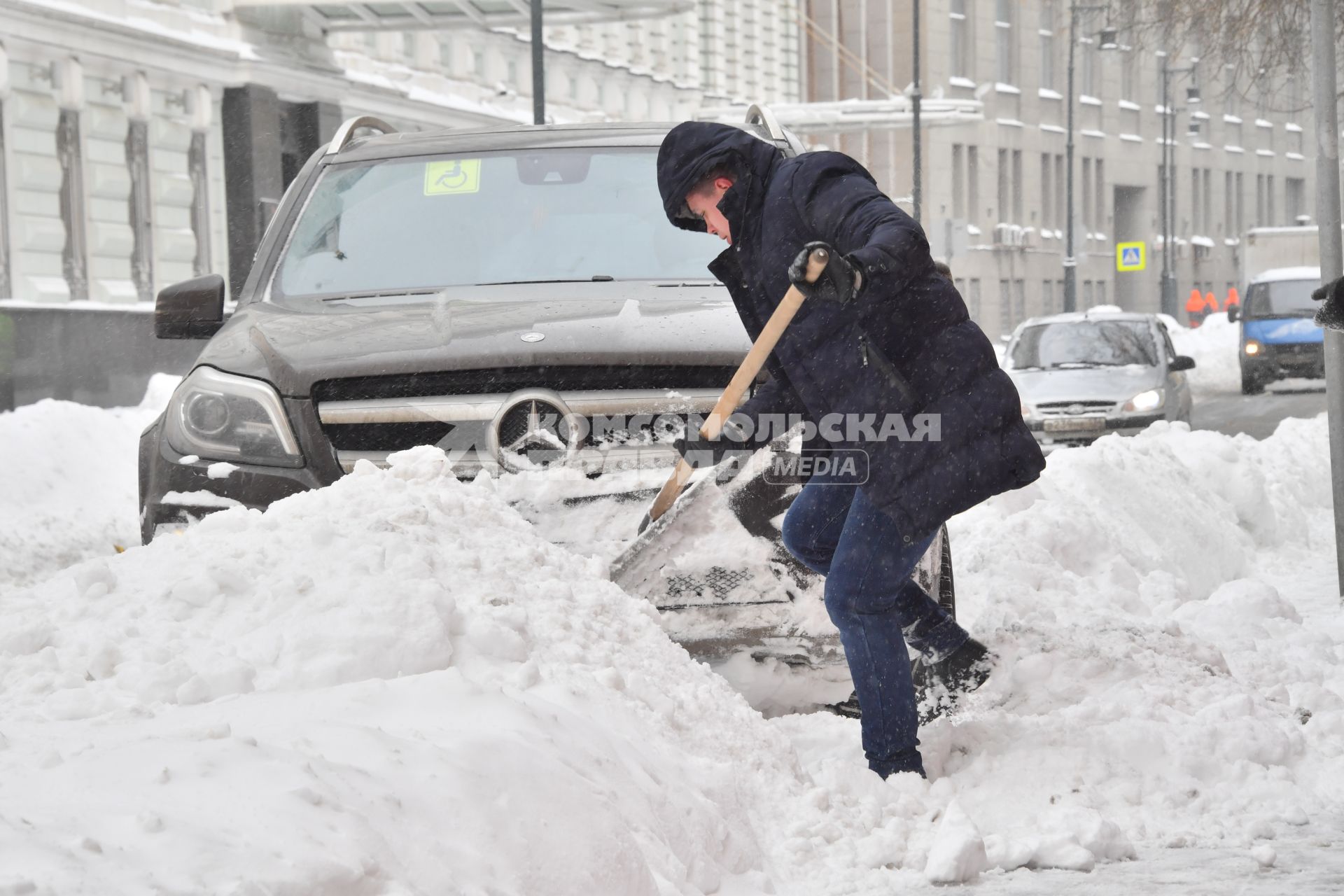 Москва. Мужчина расчищает дорогу возле автомобиля после снегопада.