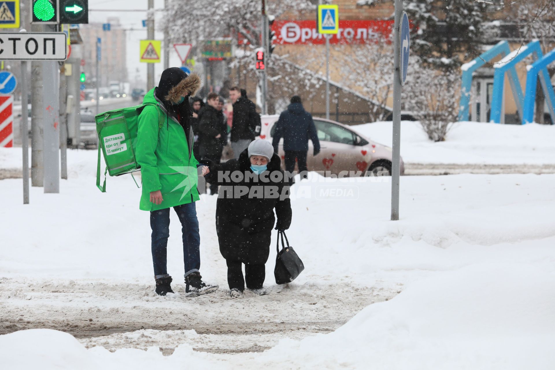 Красноярск. Юноша помогает пожилой женщине перейти дорогу, неубранную от снега.