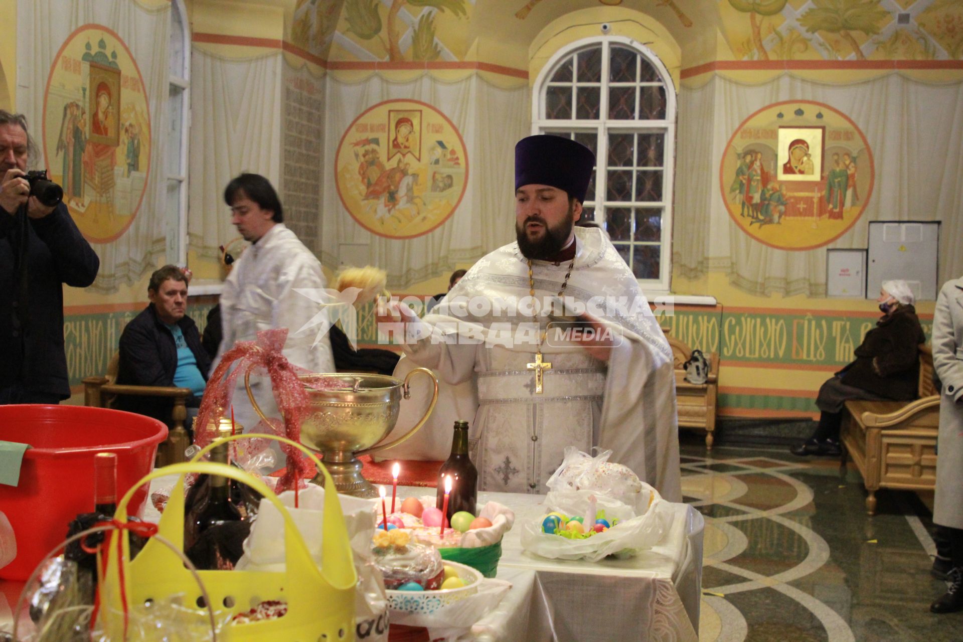 Иркутск.  Священнослужитель освящает пасхальные куличи и яйца.
