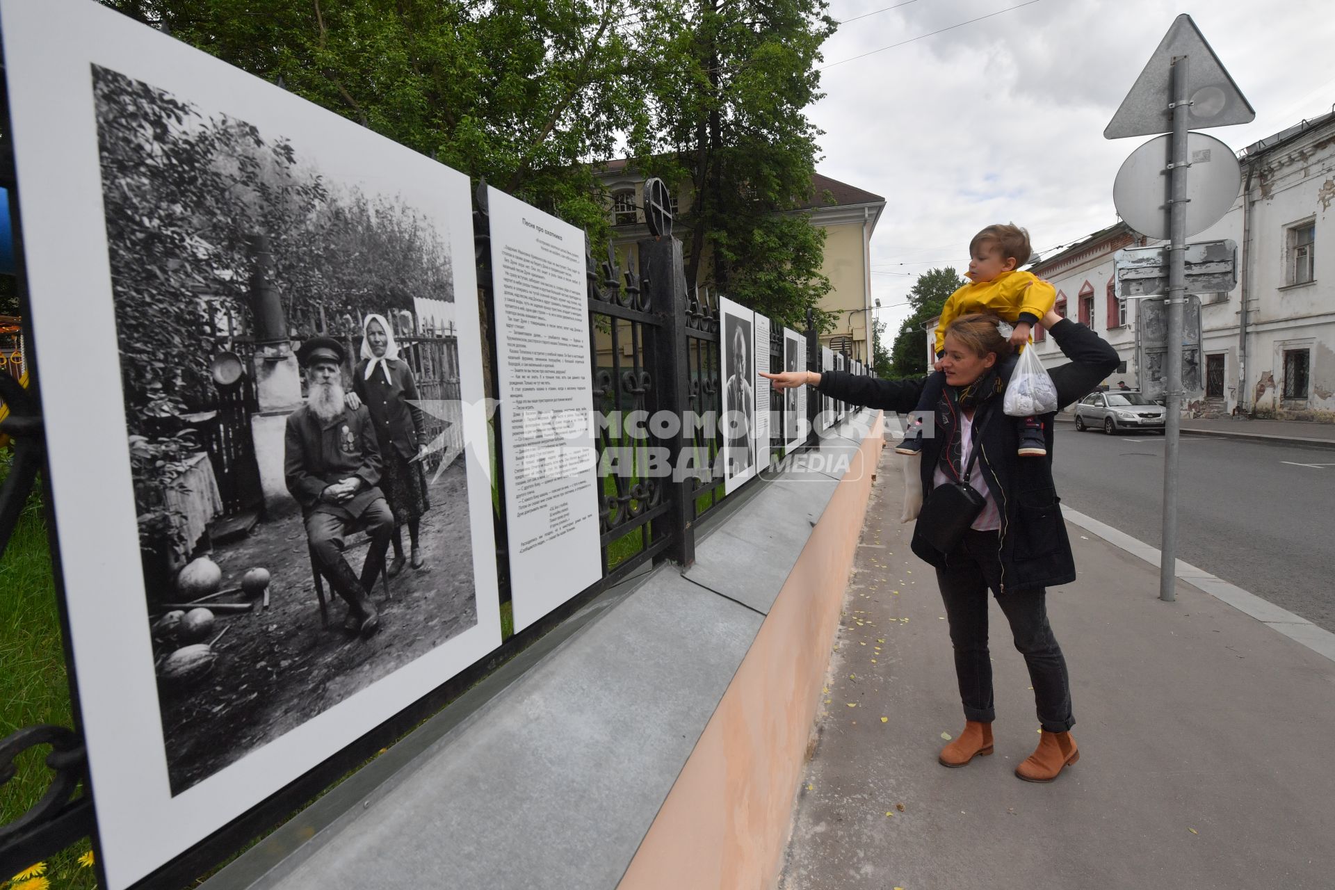 Москва.  Прохожие у фотографий  на выставке под открытым небом -  проект `Люди` журналиста и фотографа Юрия Роста , у храма Живоначальной Троицы в Хохлах .