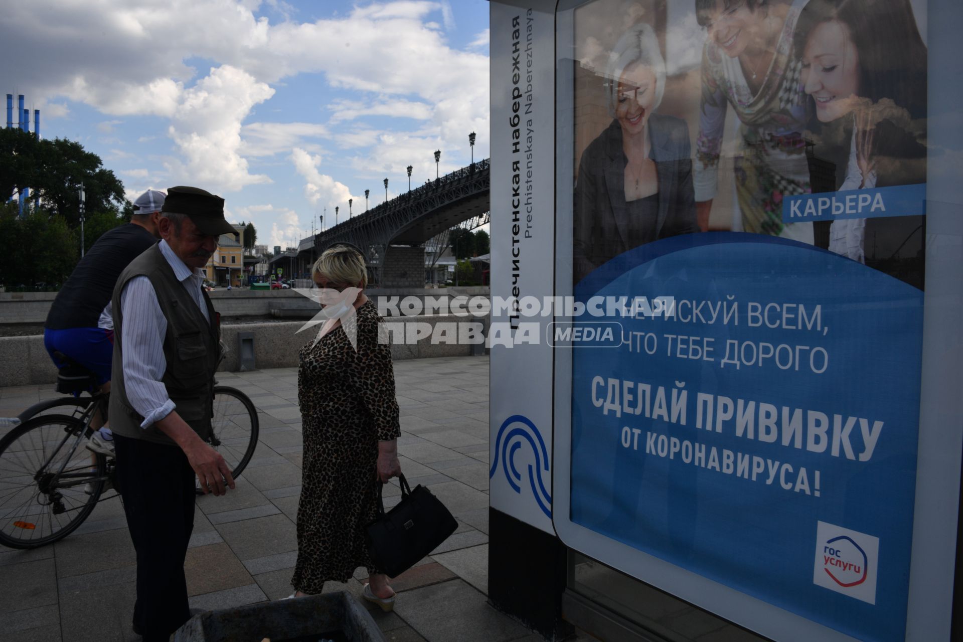 Москва. Мужчина и женщина у плаката с призывом сделать прививку.