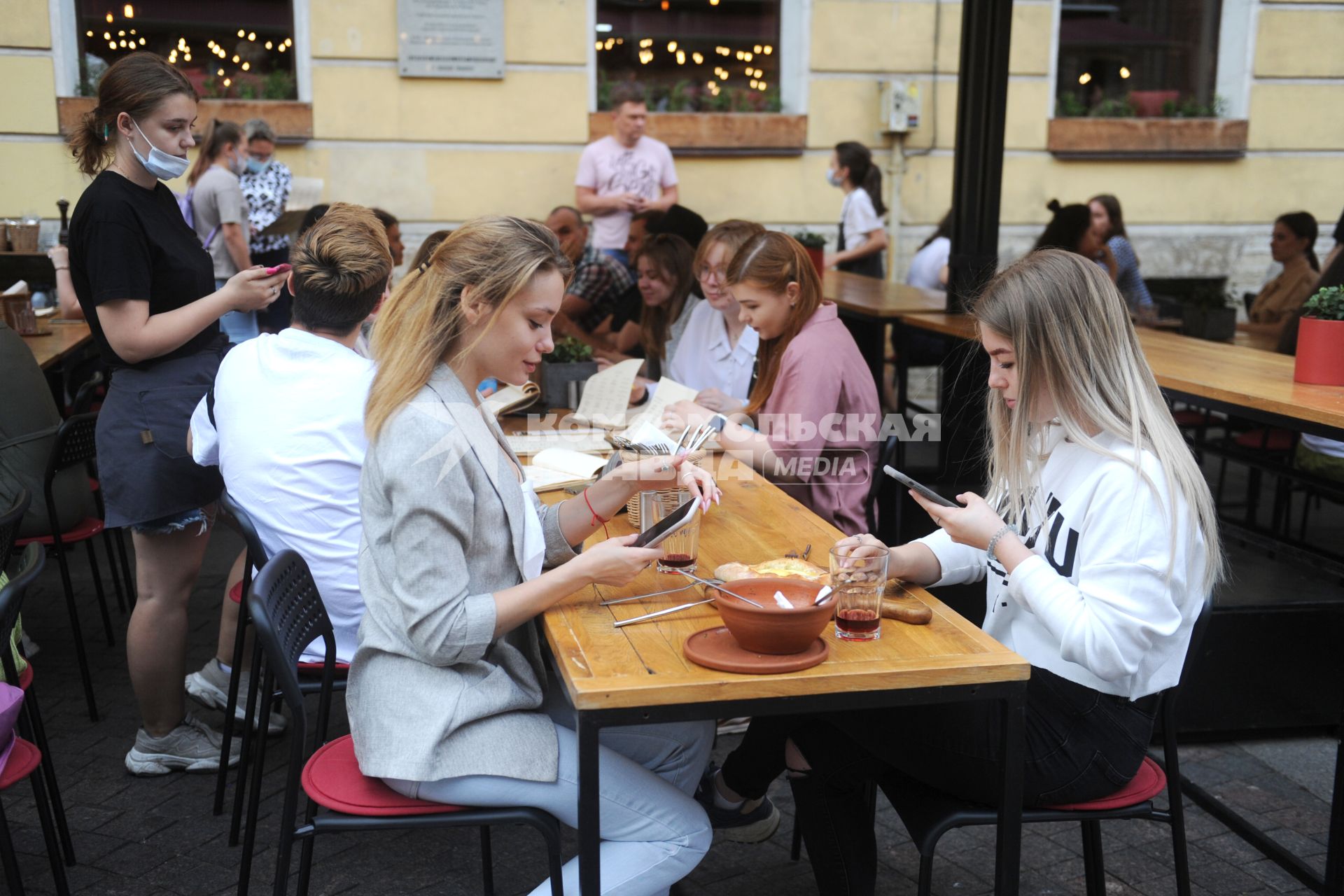 Санкт-Петербург. Девушки с мобильными телефонами сидят за столиками на веранде кафе.