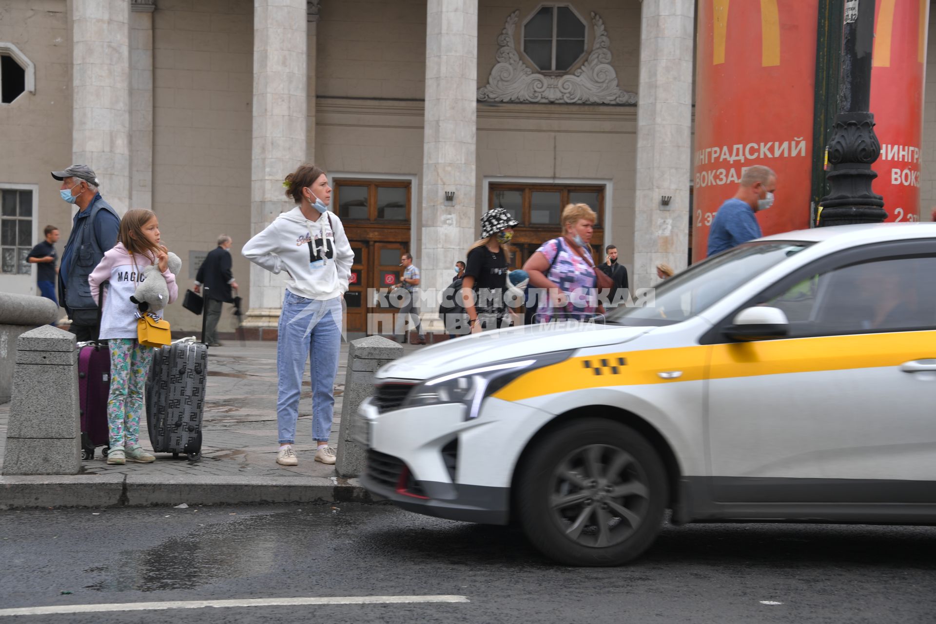 Москва. Женщина и девочка с багажом стоят на тротуаре у такси.