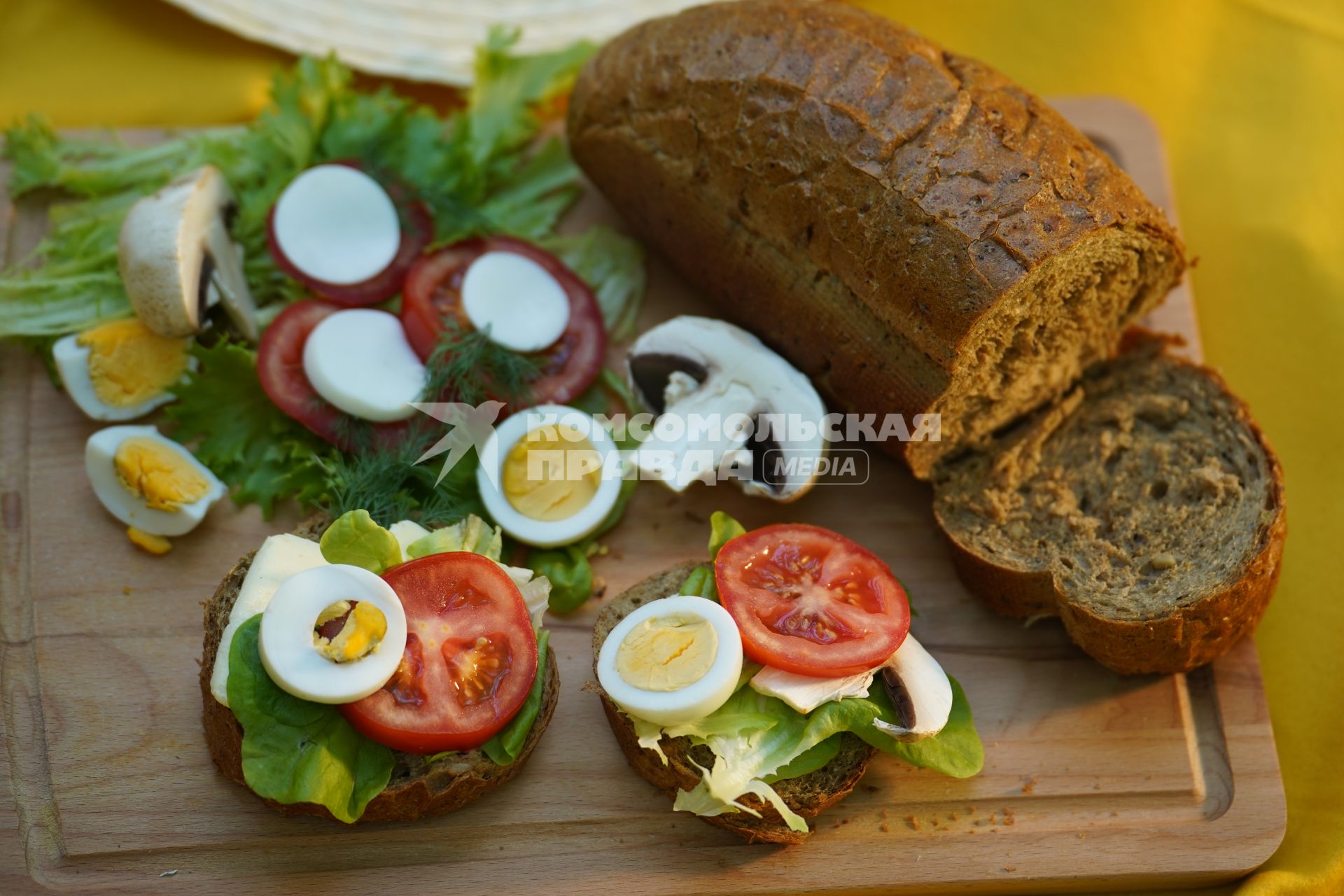 Самара. Батон ржаного хлеба, бутерброды с зеленым салатом, помидорами, моцареллой, яйцом и шампиньонами на деревянной доске.