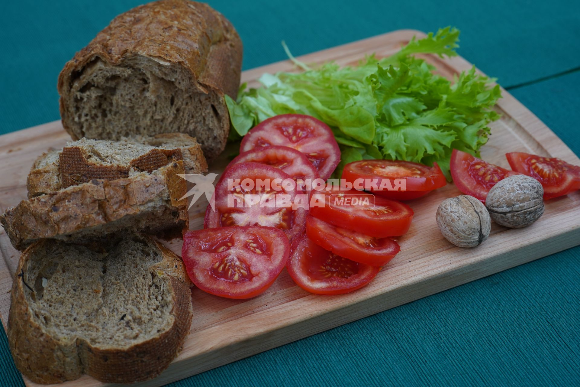 Самара. Батон ржаного хлеба, помидоры, зеленый салат и грецкие орехи на деревянной доске.