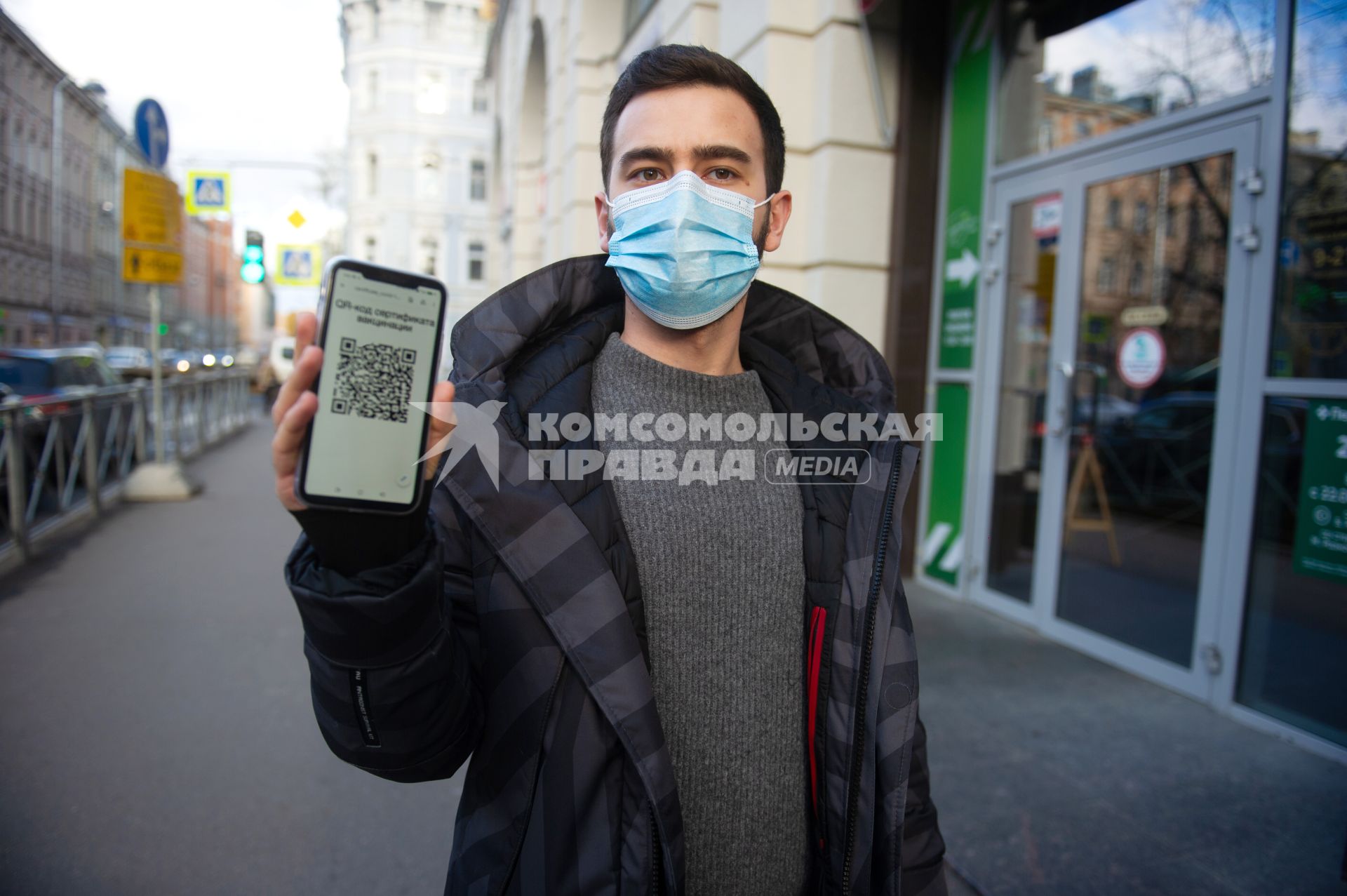 Санкт-Петербург. Юноша в маске и мобильным телефоном, на экране которого отображен QR-код, заходит в торговый центр.